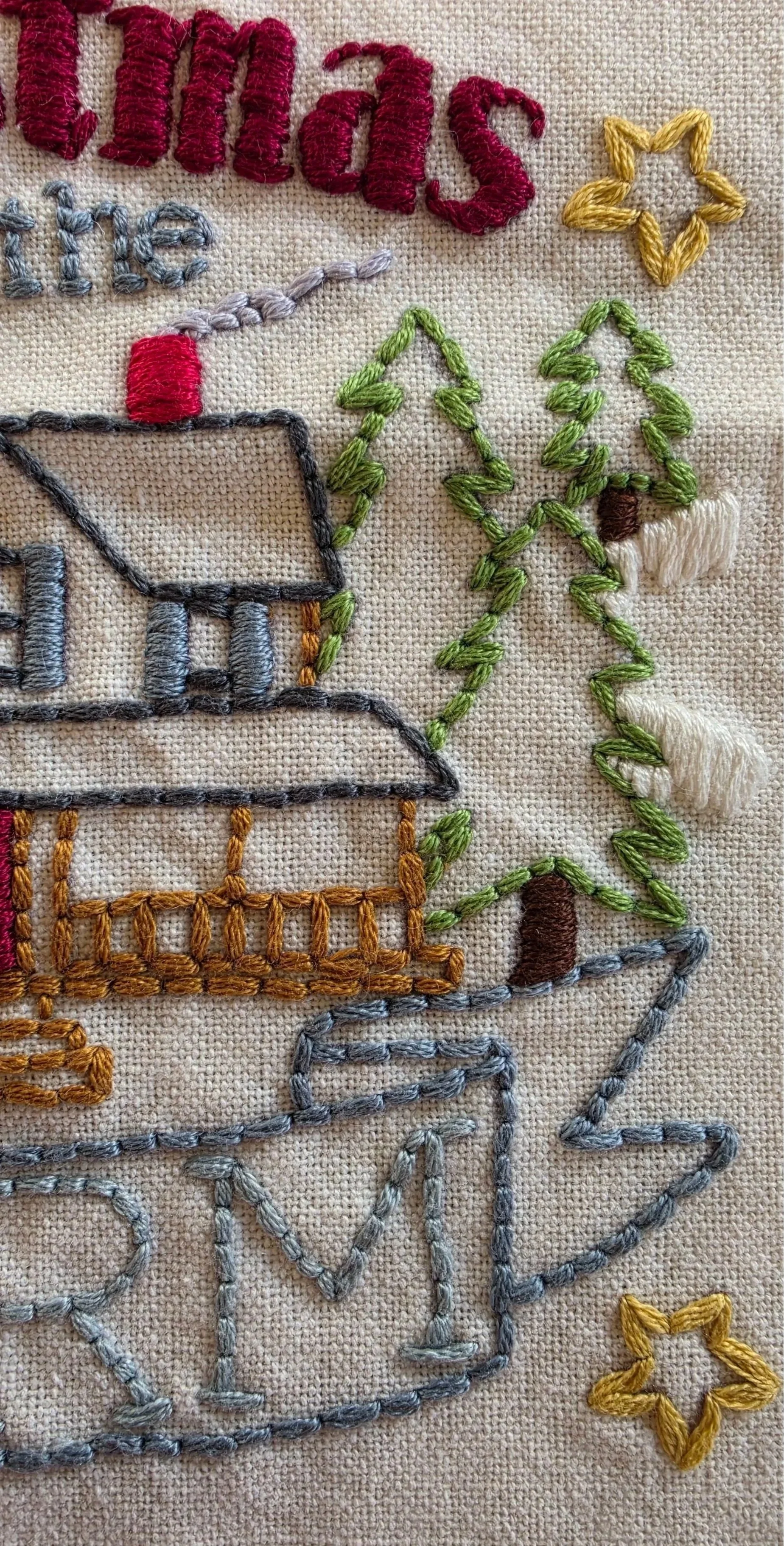 Detailed view of hand-embroidered farmhouse windows, roof, and evergreen details in the Christmas design.