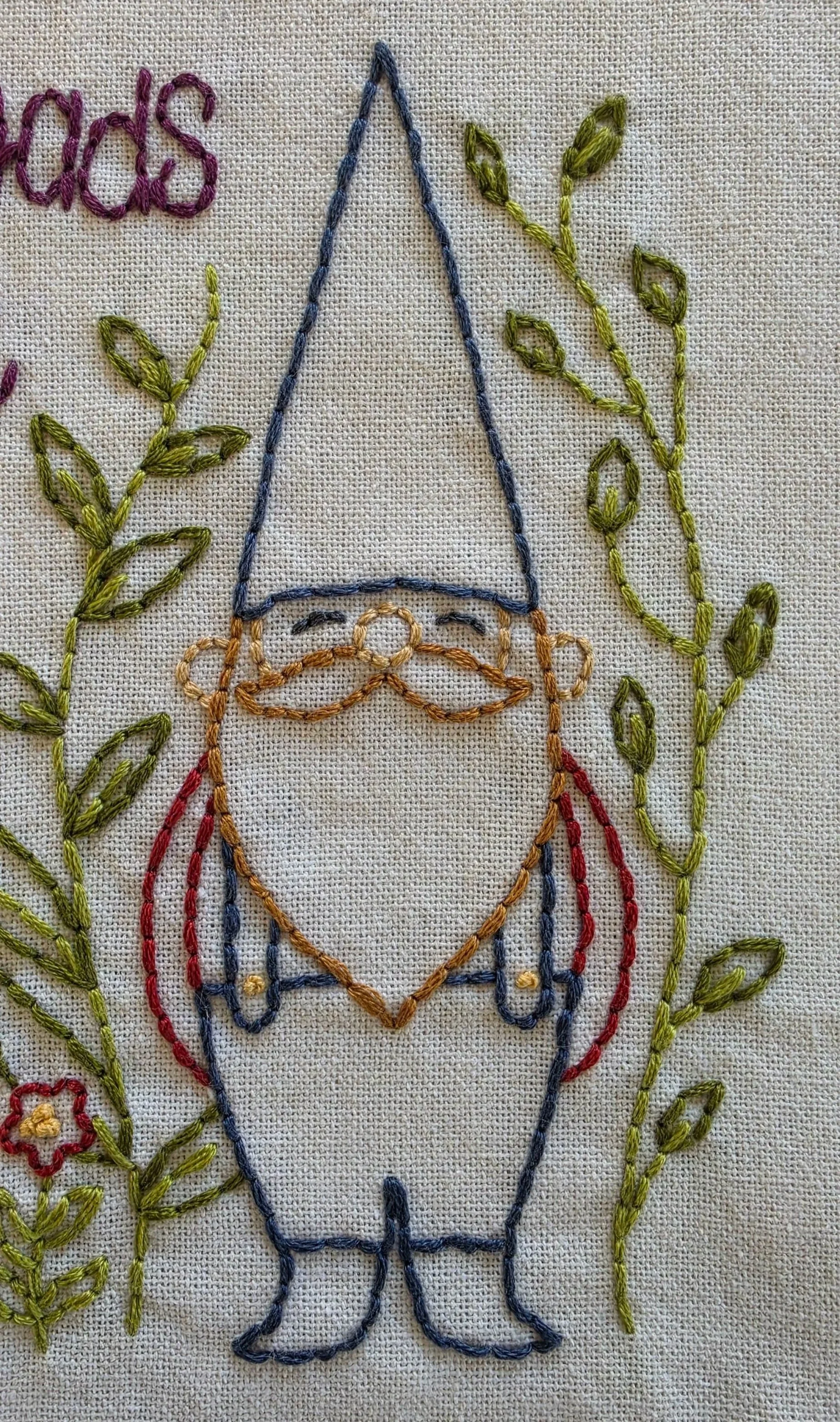 Detailed view of the colorful hand-embroidered wildflowers and green leaves beside the country gnome.