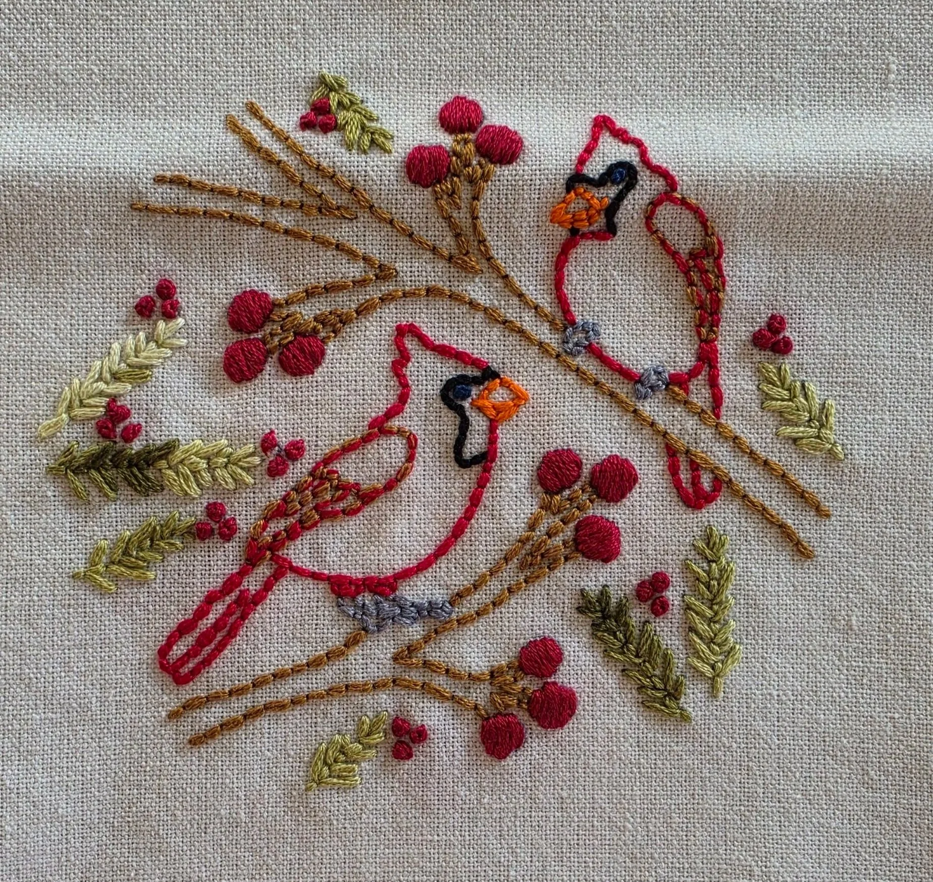 Full view of hand-embroidered cardinals, leafy branches, and red berries on natural-colored towel fabric.