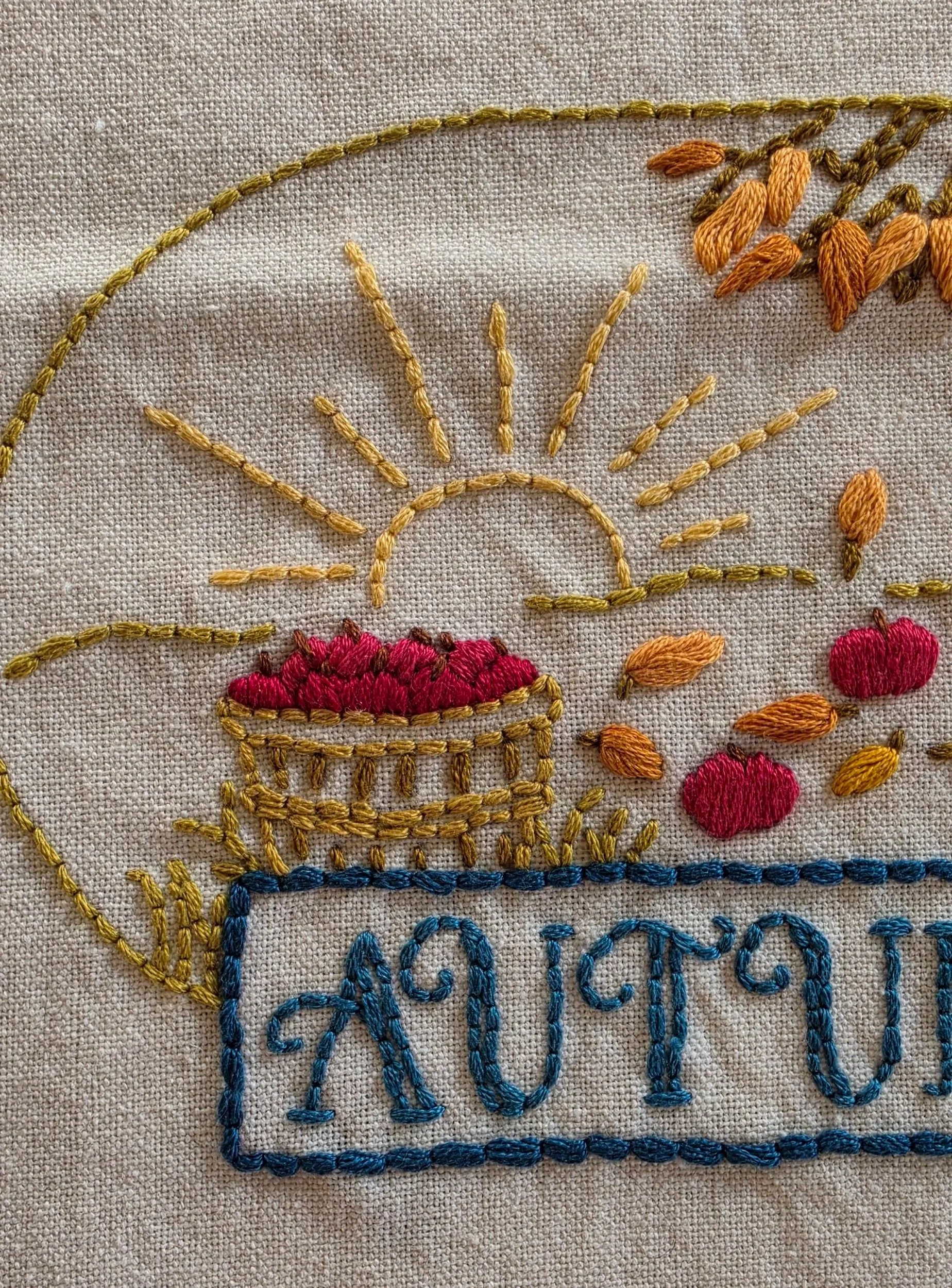 Close-up of the golden embroidered sun and basket of red apples on the autumn kitchen towel.