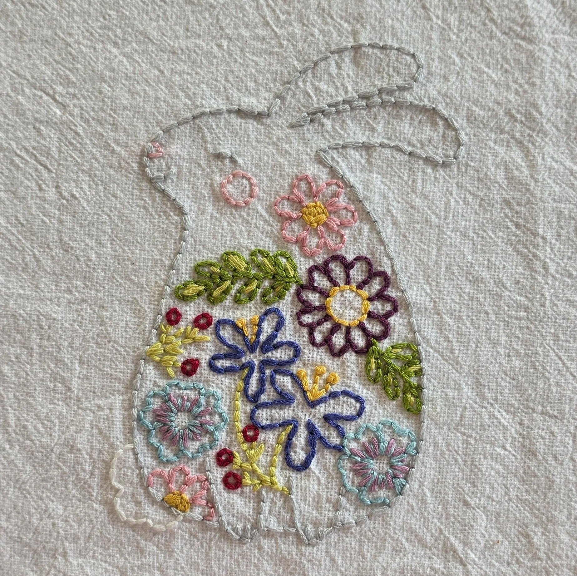 Full view of a hand-embroidered bunny silhouette decorated with colorful flowers and green leaves on a white towel.
