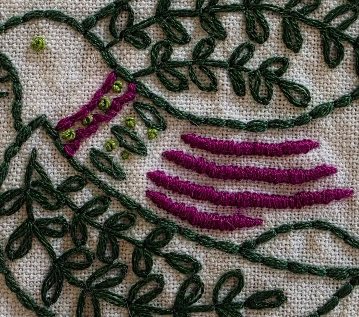 Close-up of green and plum hand embroidery on a bird design kitchen towel.