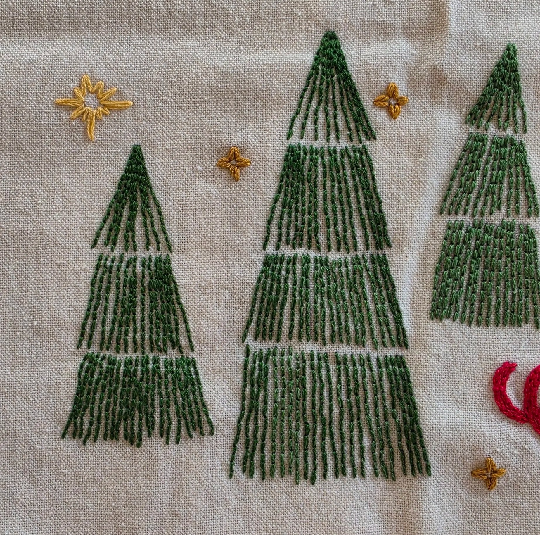 Close-up of three green embroidered evergreen trees with delicate decorative stitching on a cotton towel.