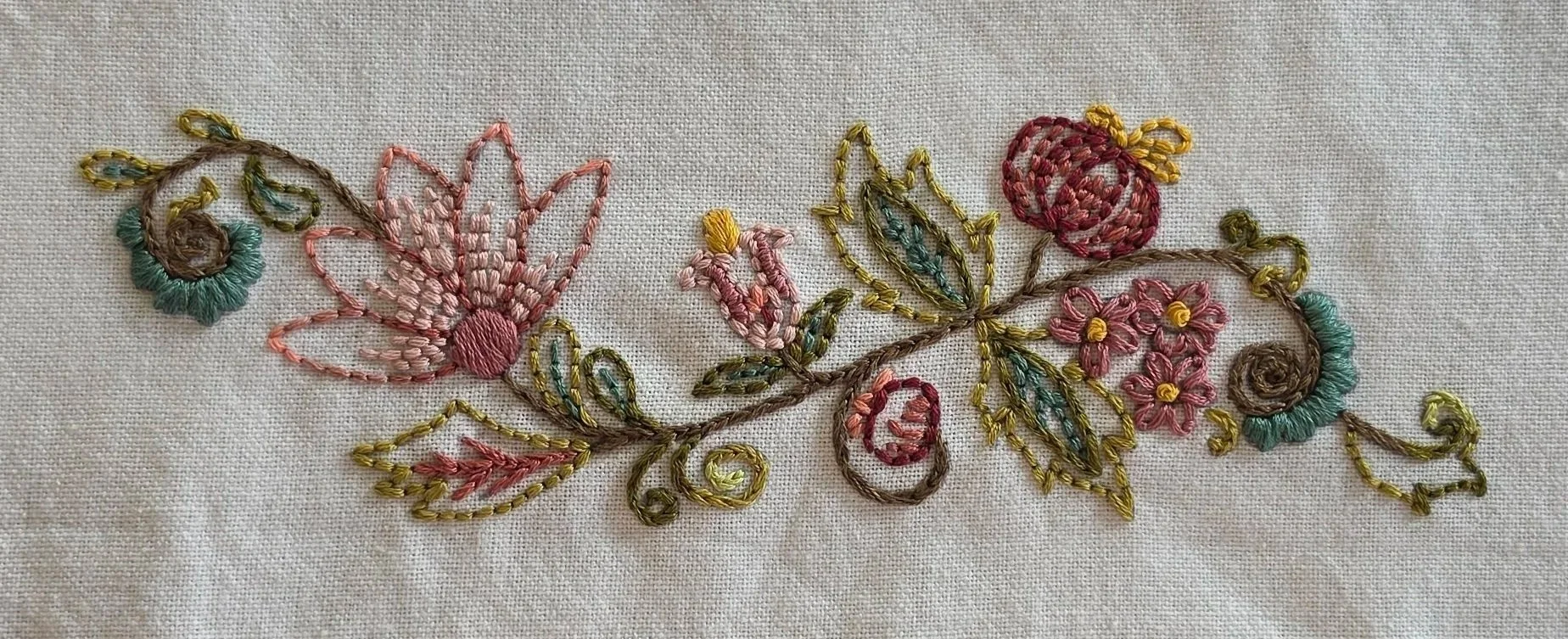 Full floral vine embroidery with pink and burgundy flowers, teal accents, and green leaves on a cream kitchen towel.