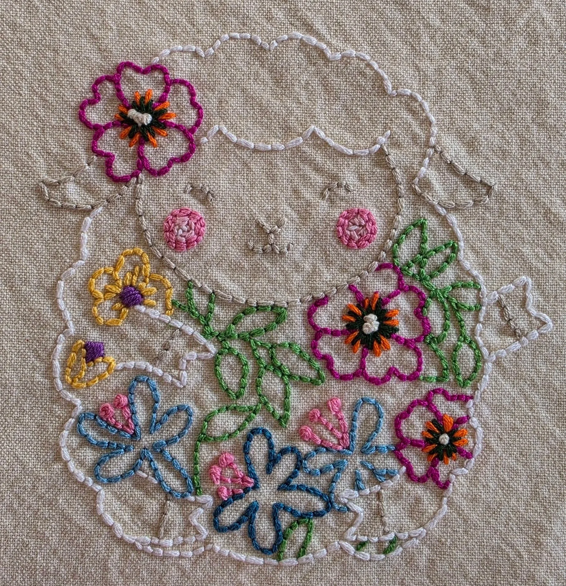 Close-up of the lamb’s embroidered face, pink cheeks, and colorful flowers stitched with embroidery floss.