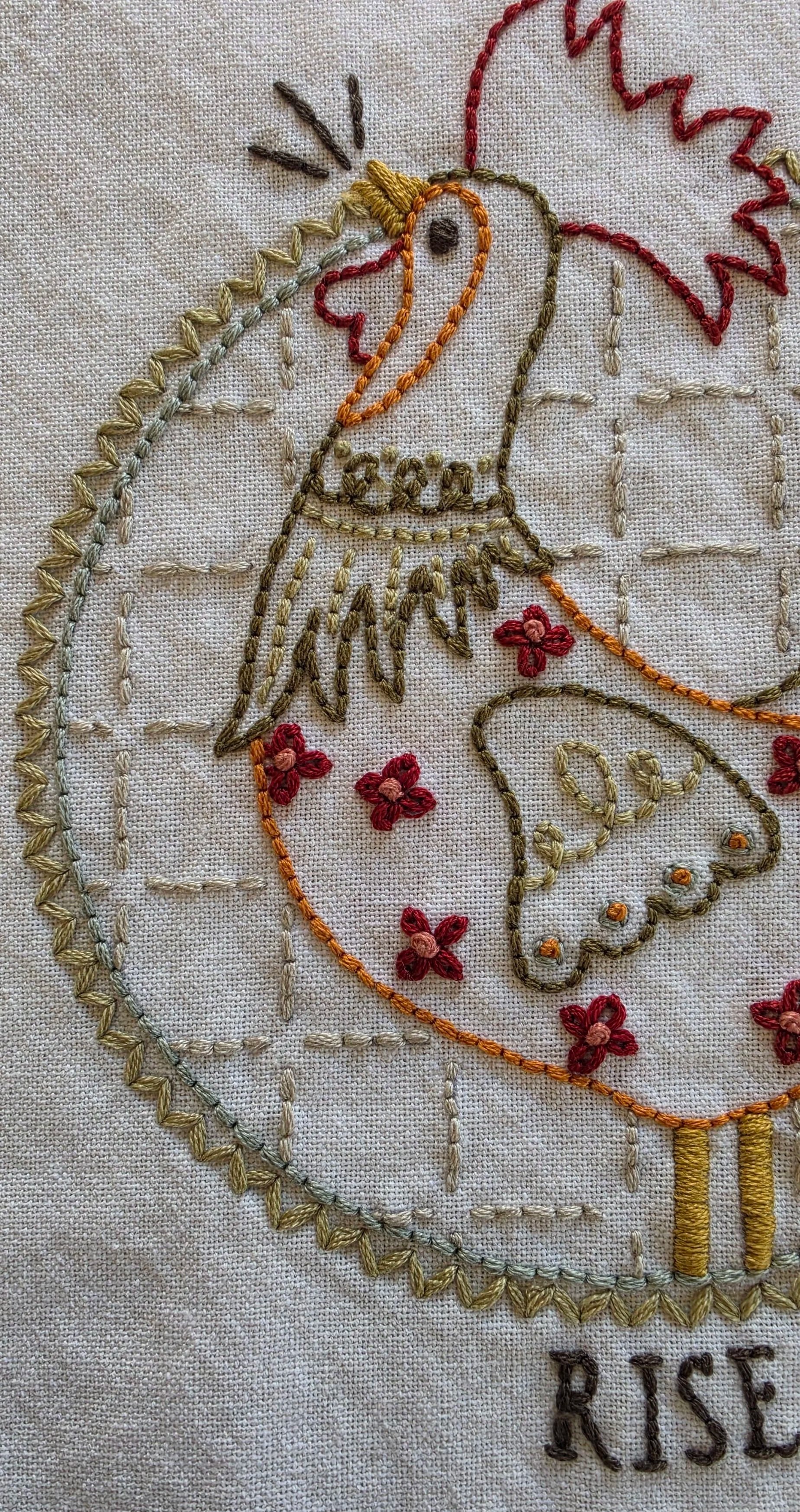 Hand-embroidered Rise & Shine rooster design with colorful folk-art stitching on a cream kitchen towel.