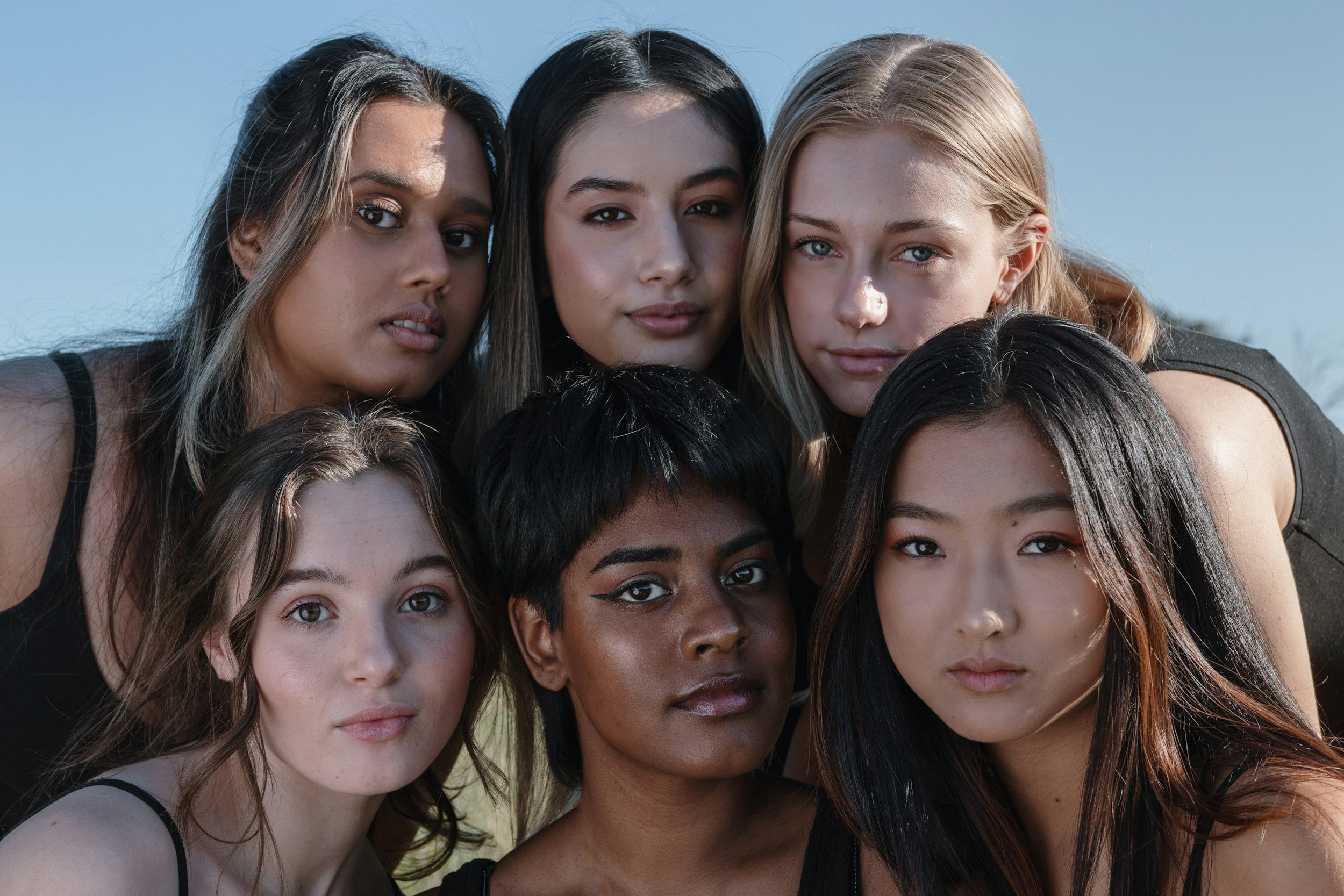 Group of seven diverse young women outdoors, closely grouped and looking at the camera.