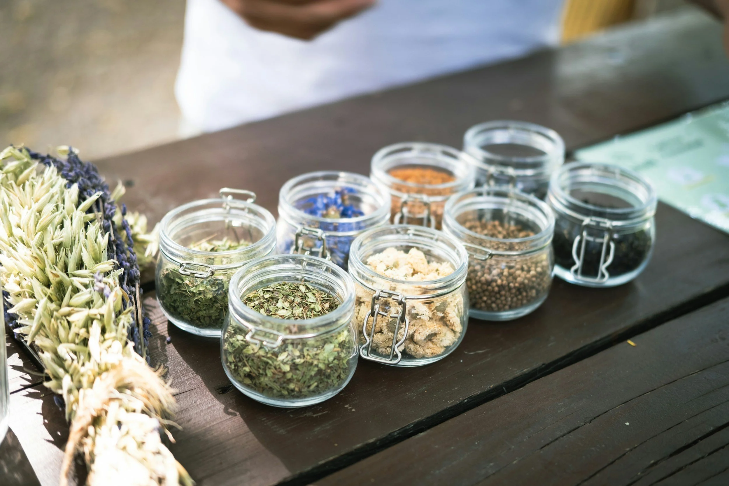 Various jars of dried herbs and spices displayed on a wooden table.