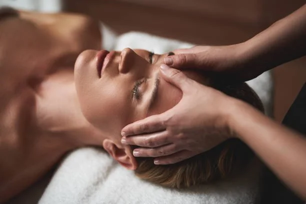 Person receiving a facial massage with closed eyes, lying on a massage table.