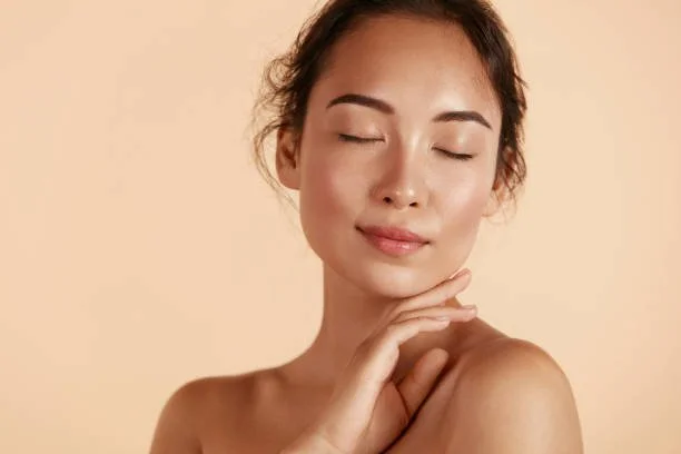A woman with closed eyes touching her shoulder gently against a beige background.