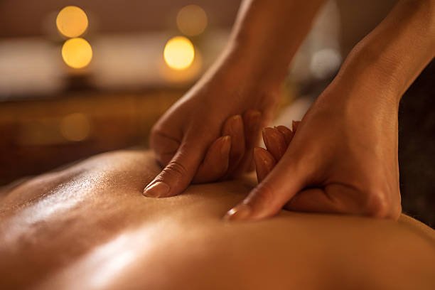 Close-up of a massage therapist's hands giving a back massage in a dimly lit room.