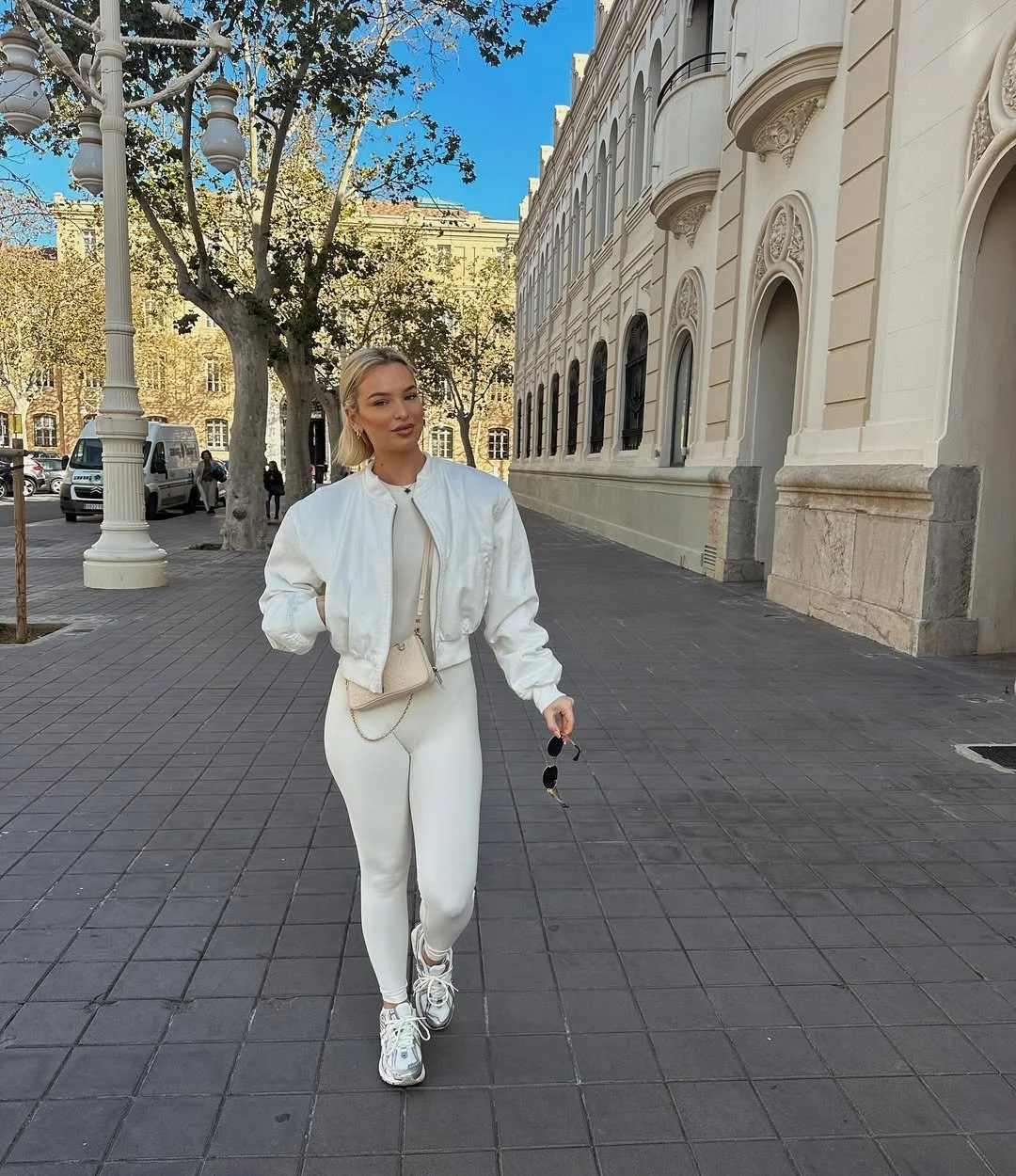 Fabia Lucia, UK fashion and lifestyle influencer represented by The New Creative Agency, wearing white athletic wear on a European city street.