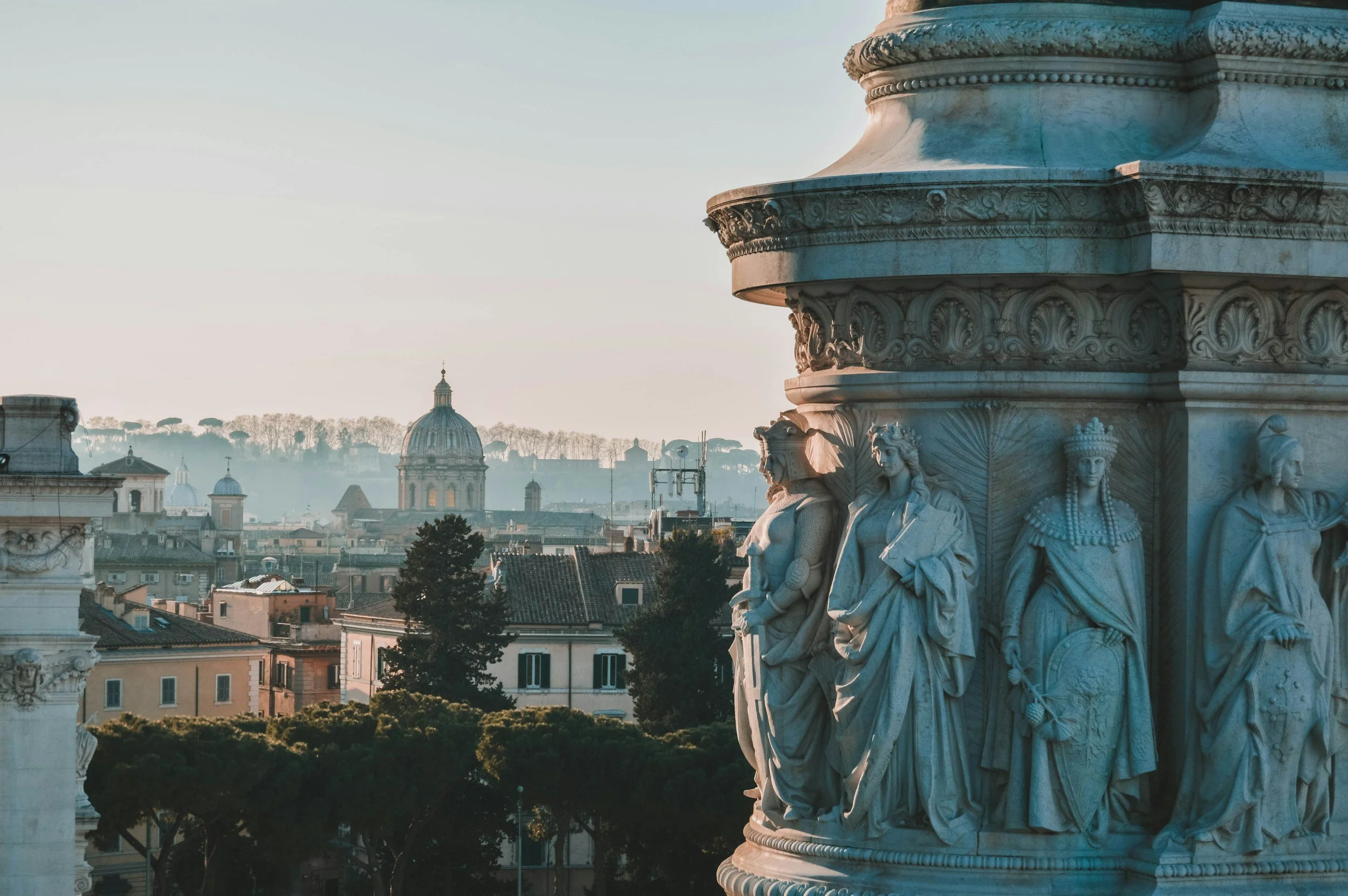 Close-up of marble sculptures on a historical monument with a cityscape and dome in the background