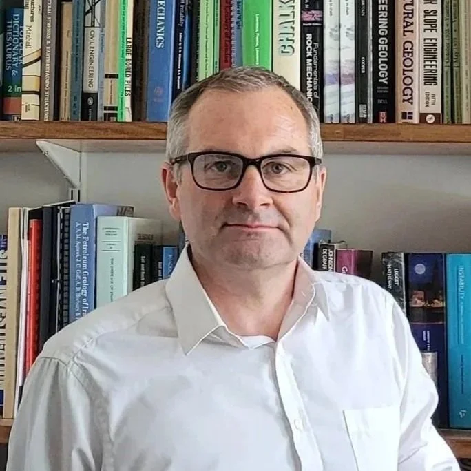 Dr James Lawrence, Chief Executive Officer (CEO) and co-director of Ground Evolution Monitoring, wearing glasses and a white shirt standing in front of bookshelves filled with books.