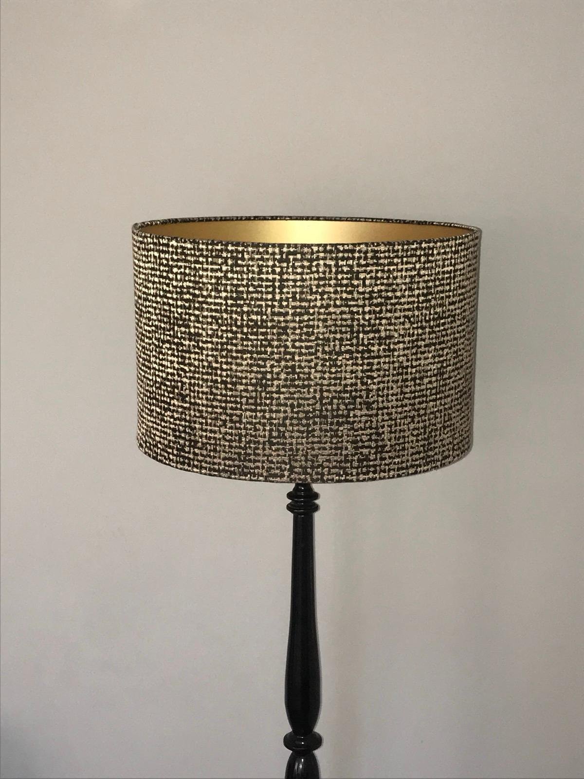 A floor lamp with a black stand and a beige and black patterned lampshade against a plain white wall.