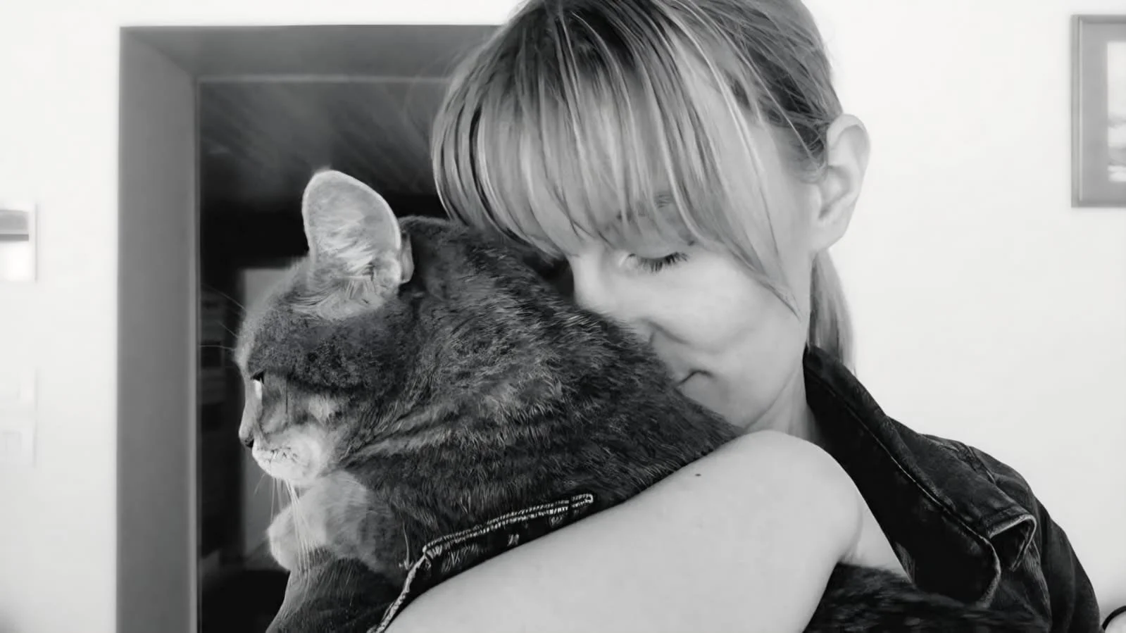 Une femme en noir et blanc tient un chat gris mouillé contre elle, dans une étreinte chaleureuse.
