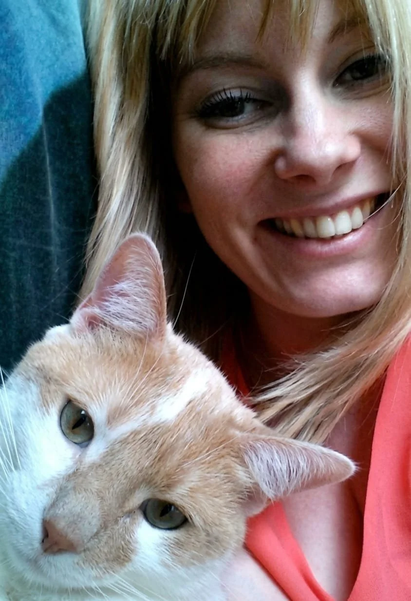 Une femme souriante avec un chat roux et blanc sur sa poitrine