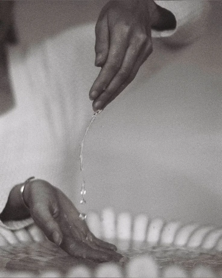 A person with a ring on their finger is pouring water from their hand into another person's hand.