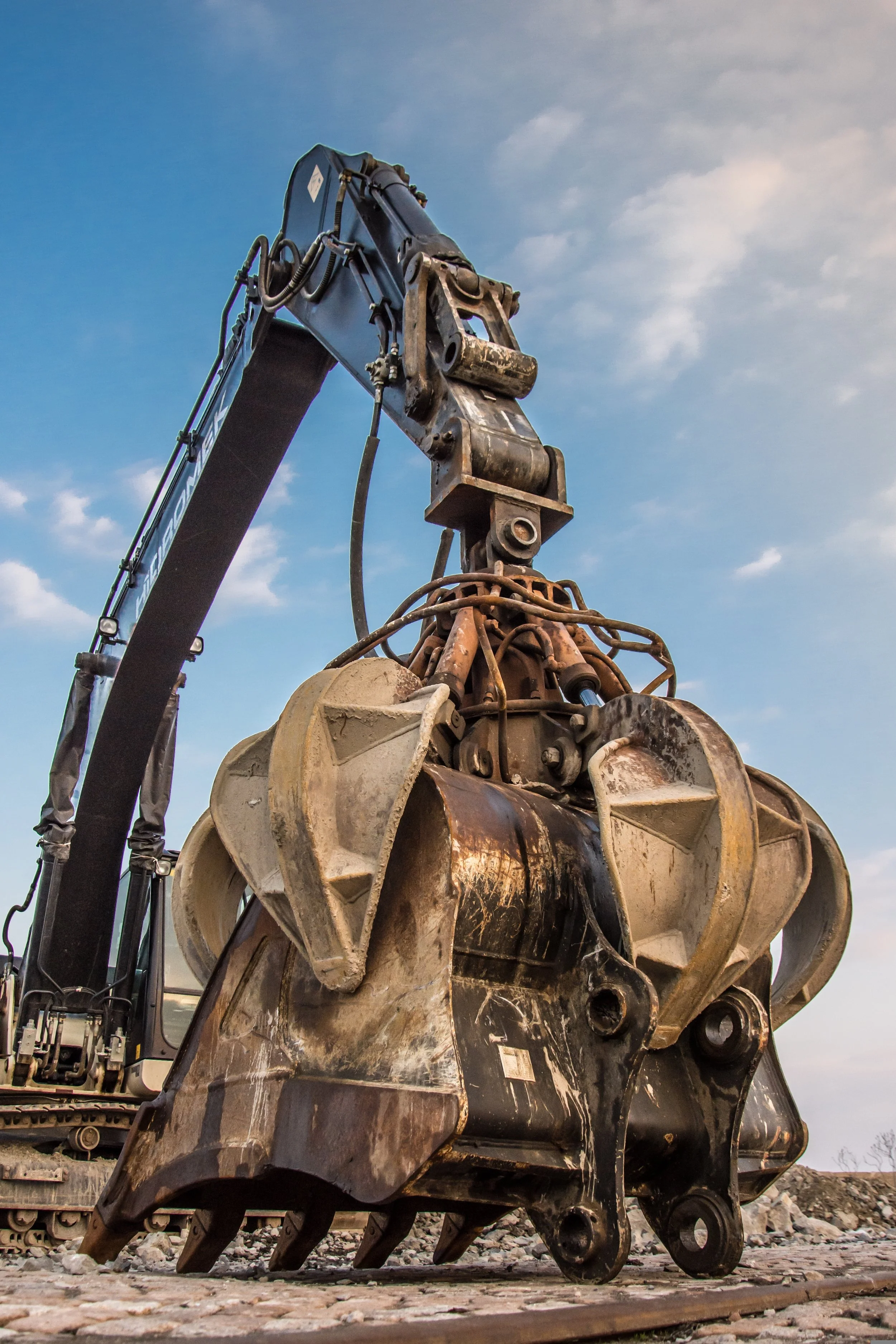 Close-up of a large excavator bucket attachment against a partly cloudy sky.