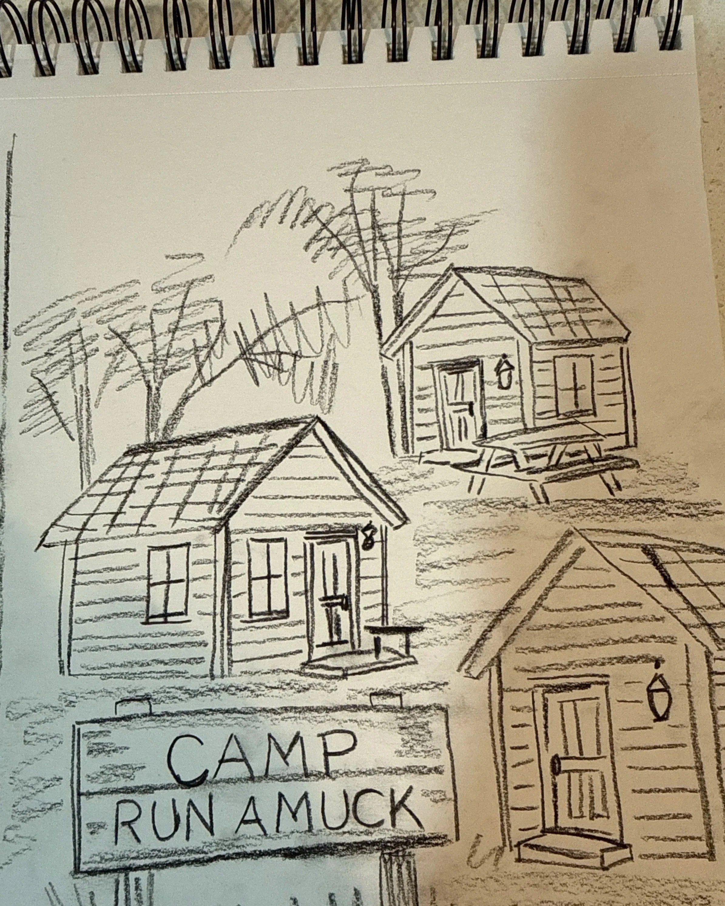A black and white sketch of three small wooden cabins, one with a porch and a picnic table, surrounded by trees. A sign reads "CAMP RUN A MUCK."