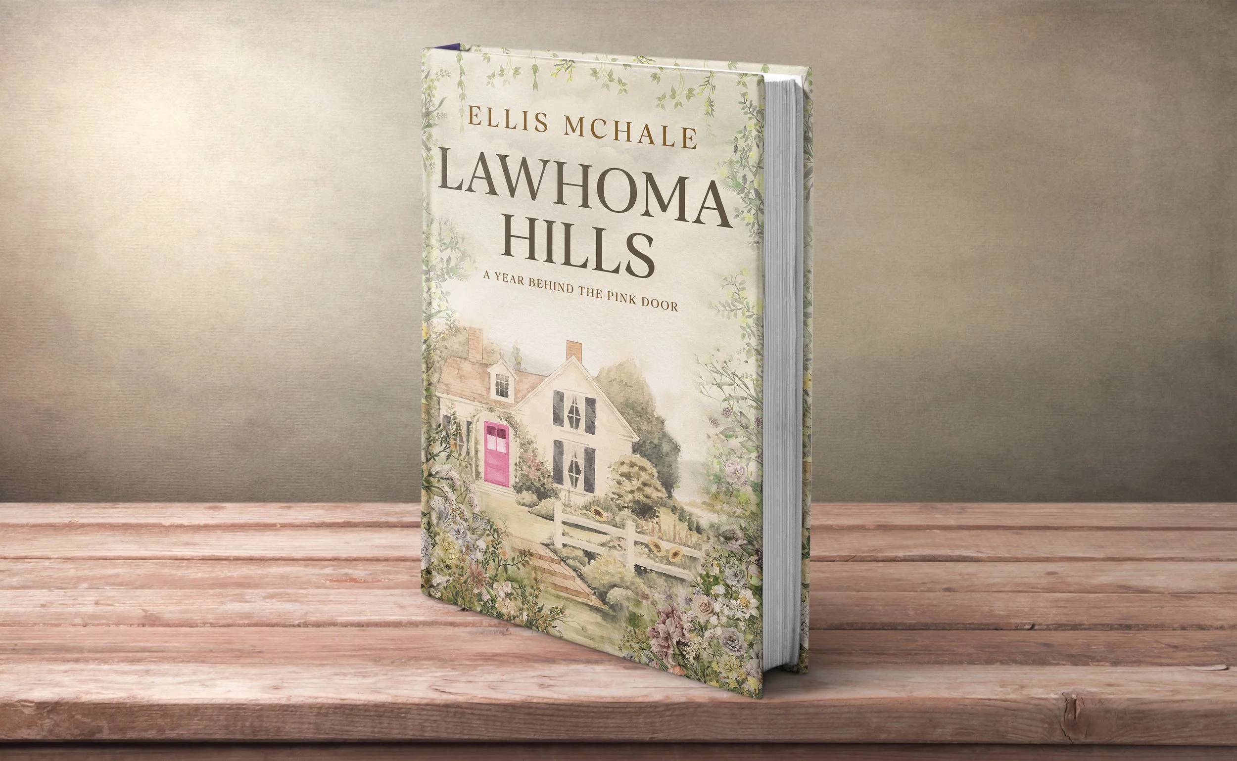 A hardcover book titled "Lawhoma Hills" by Ellis Mchale, with a watercolor illustration of a house with a pink door, surrounded by trees and flowers, on a wooden surface against a neutral background.