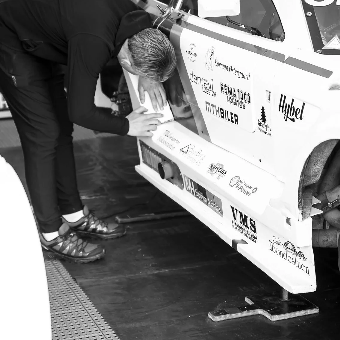 En person tjekker en racerbils front med sponsorlogos i en garage.