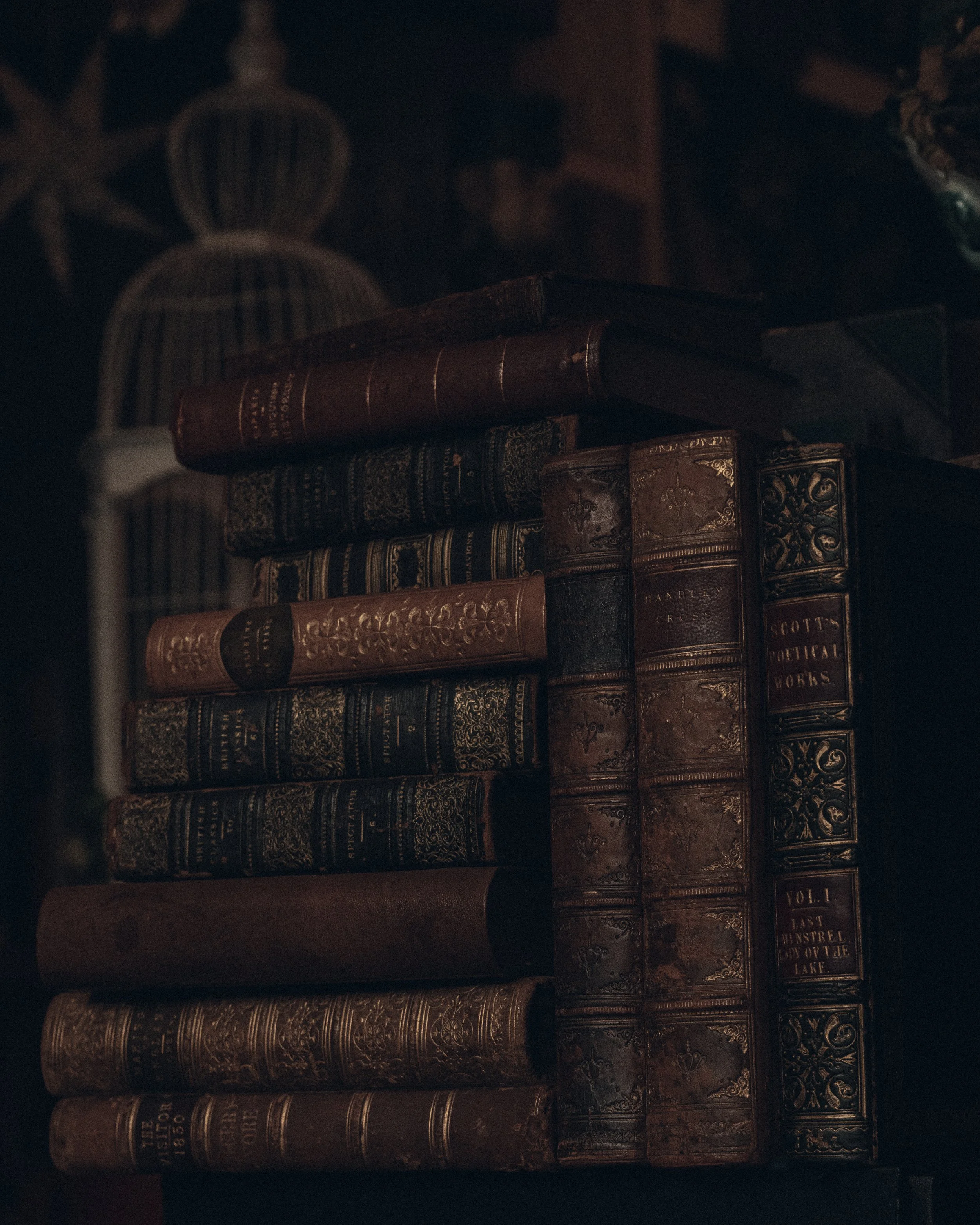 A stack of old, leather-bound books with ornate gold designs on the spines, placed on a dark shelf or table.