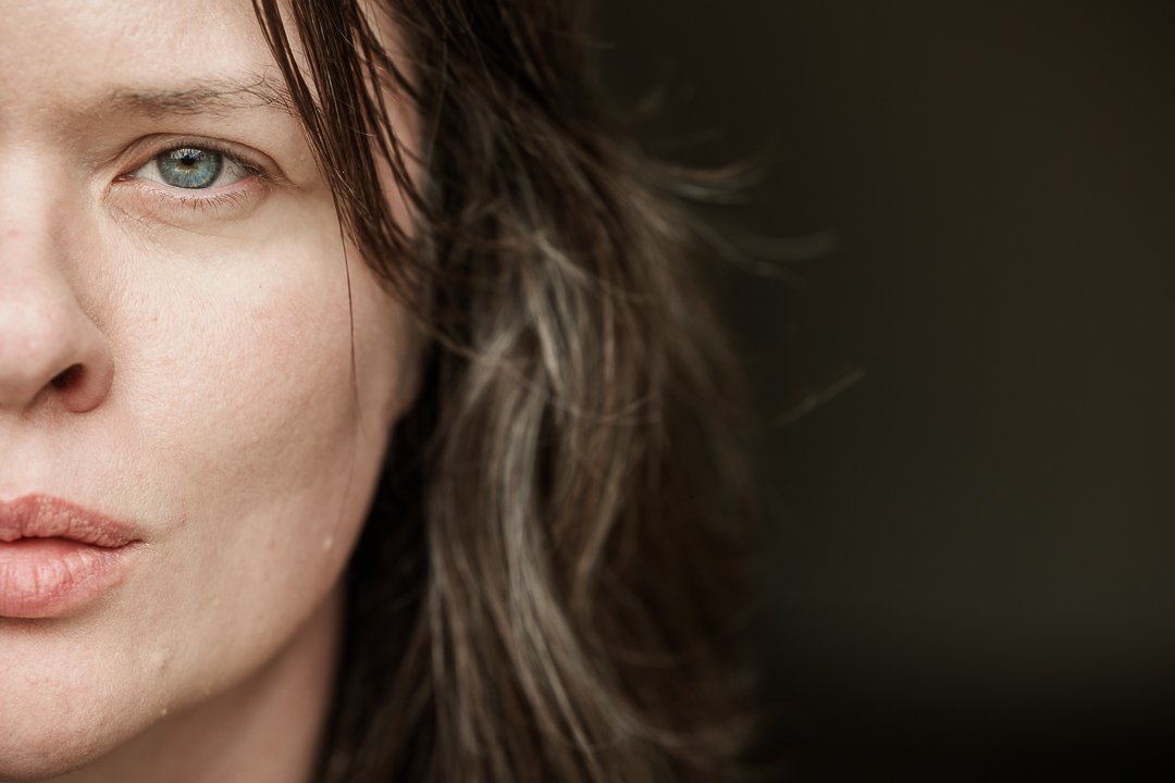 Close portrait of a woman, half her face turned into shadow and hair, one light blue eye meeting the camera.