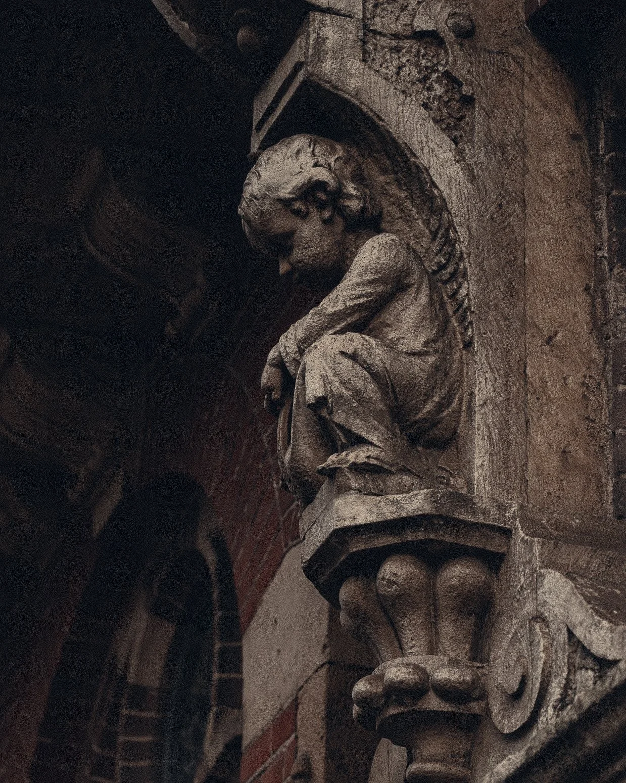 A detailed stone sculpture of a boy sitting on a ledge on a brick and stone wall, decorated with ornate carvings.