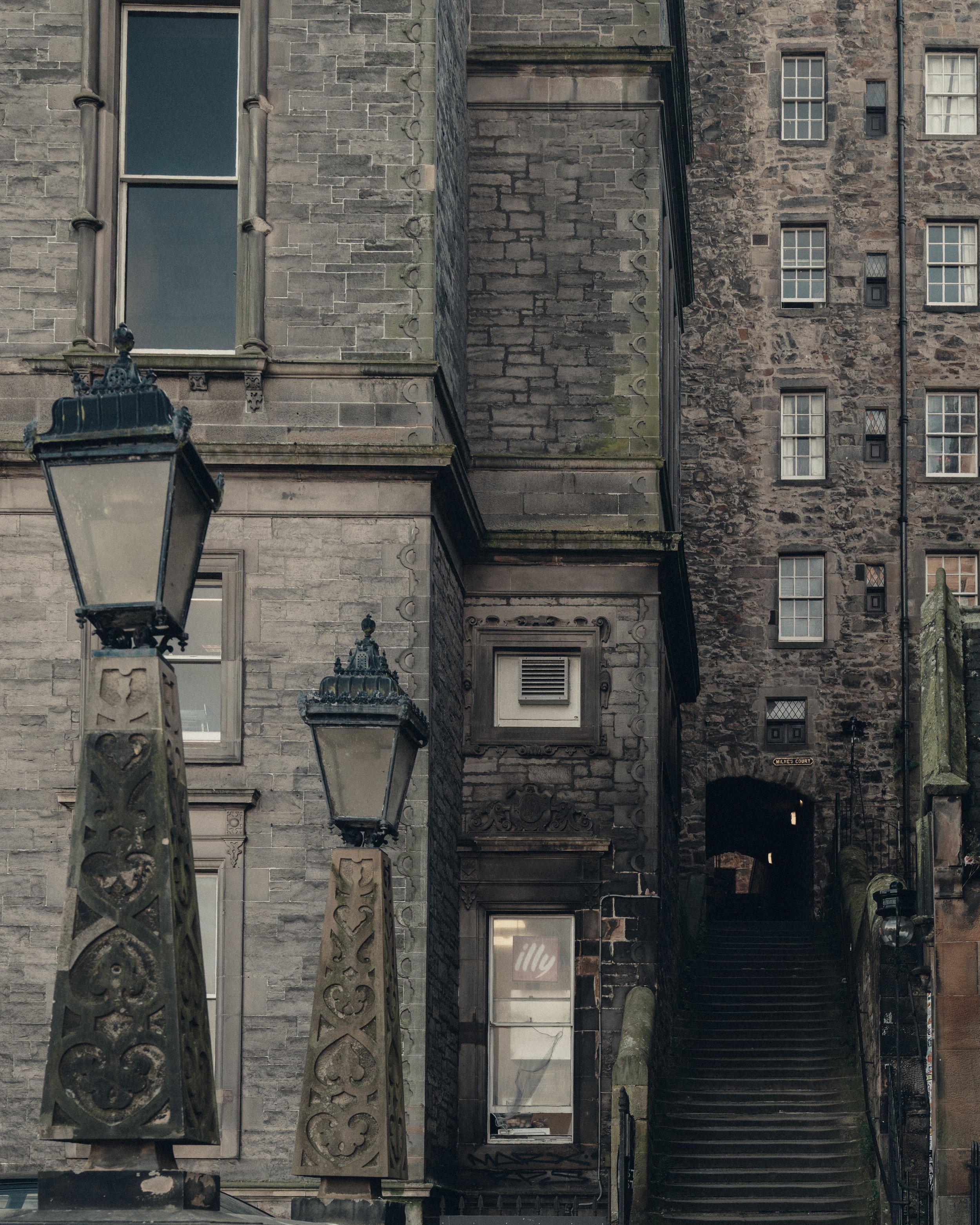 An urban scene featuring stone buildings, ornate street lamps, and a staircase leading upstairs in a historic area.