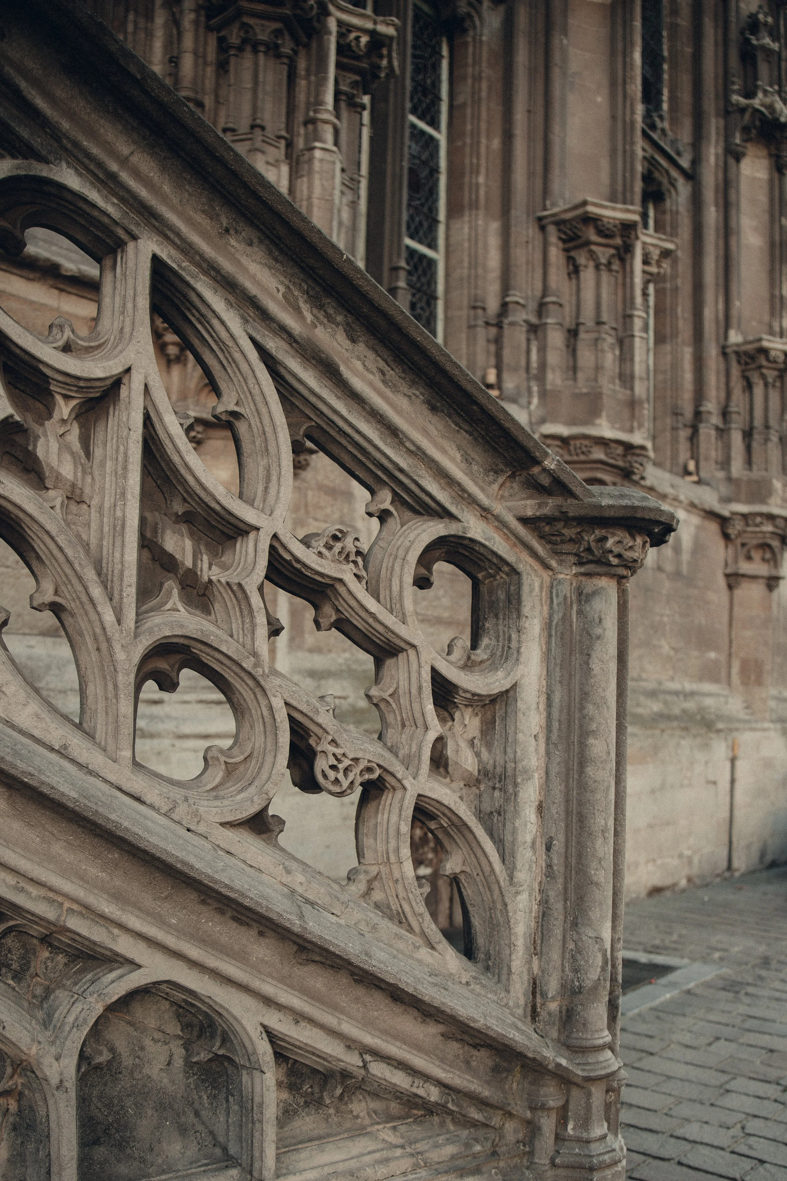 Close-up of an ornate stone railing on a historic building, likely a church or cathedral, with detailed carvings and large windows in the background.