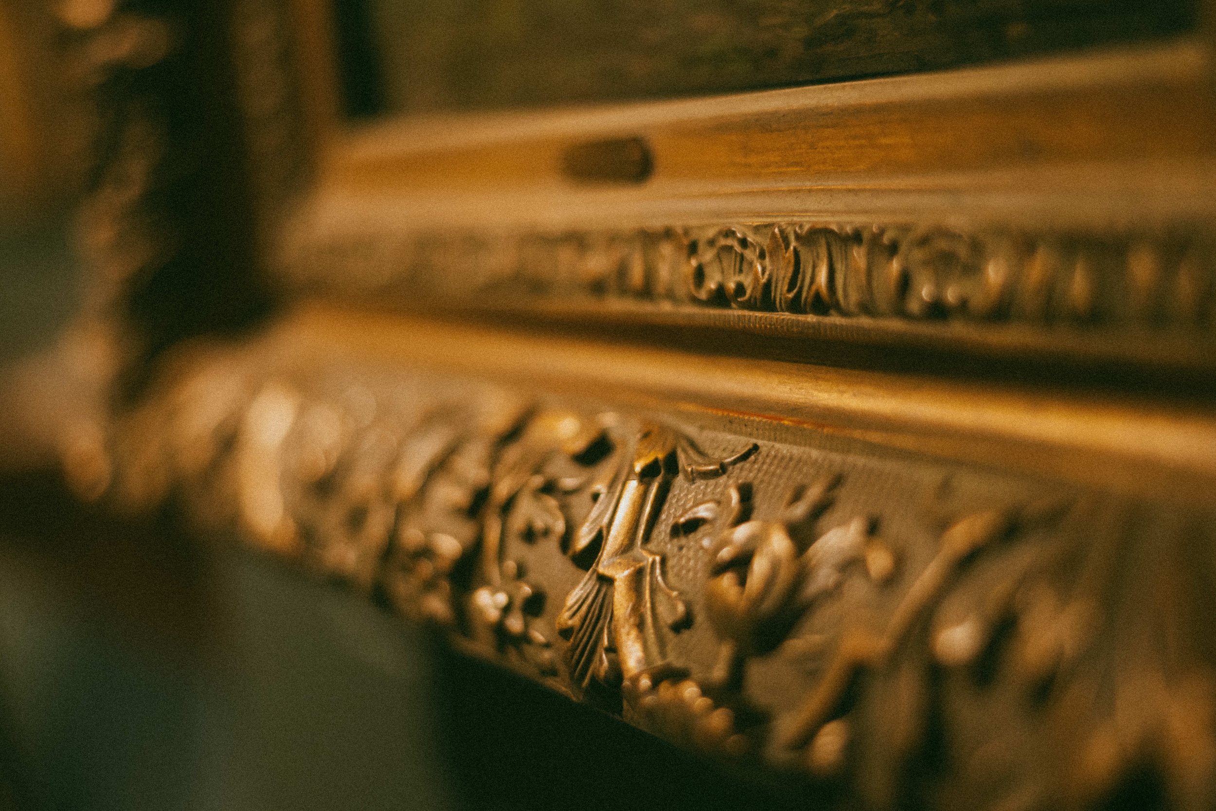 Close-up of ornate gold-colored decorative trim on wooden furniture.