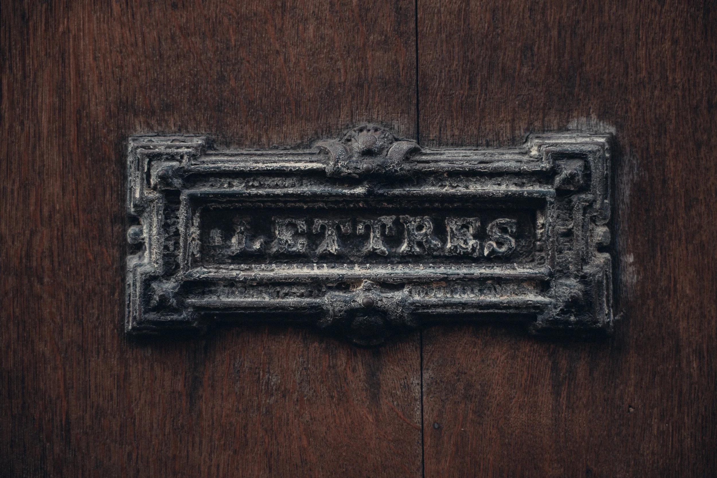 A vintage letter slot labeled 'LETTERS' on a dark wooden door.