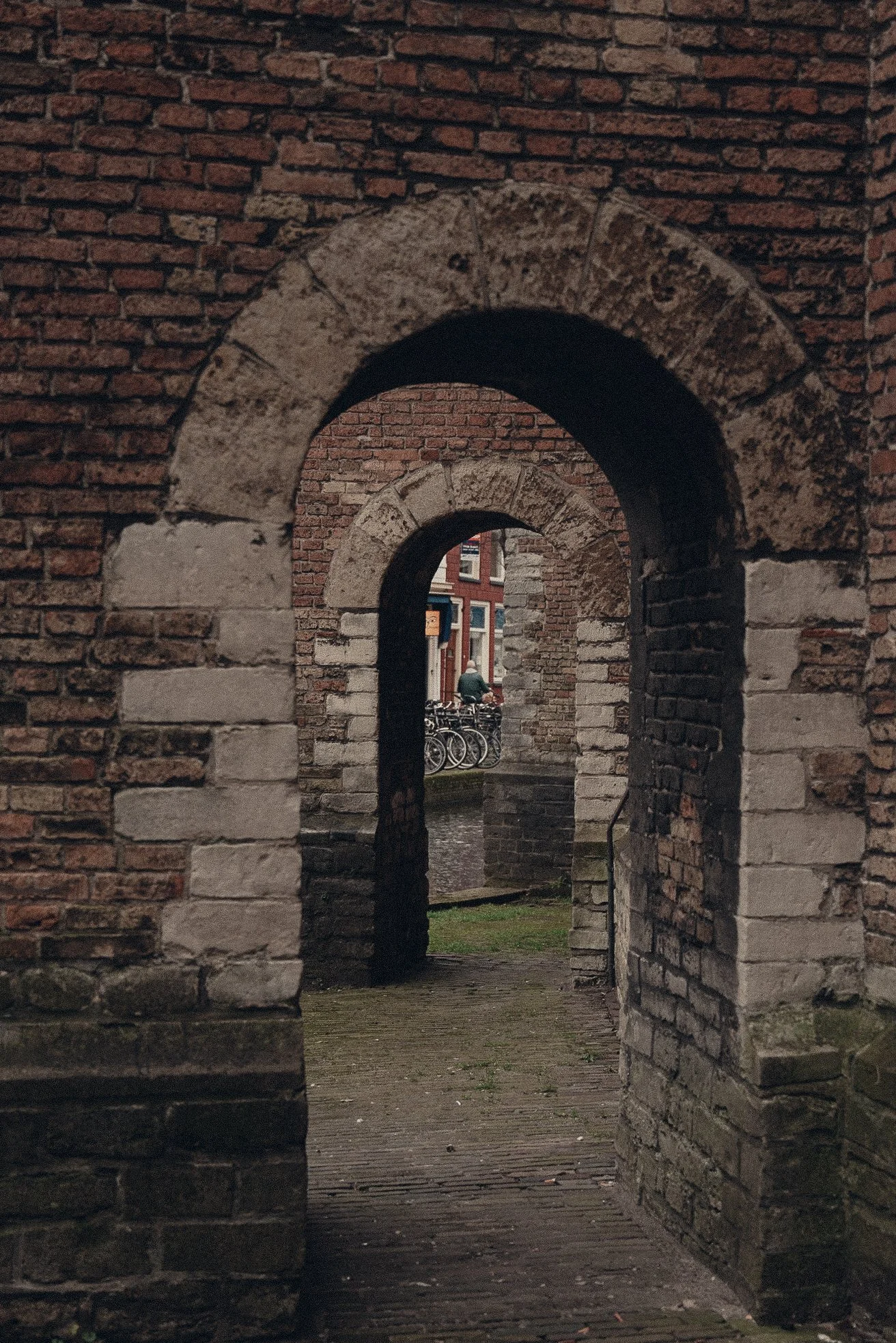 View through a series of brick archways showing a person on a bicycle and part of a street scene in the background.