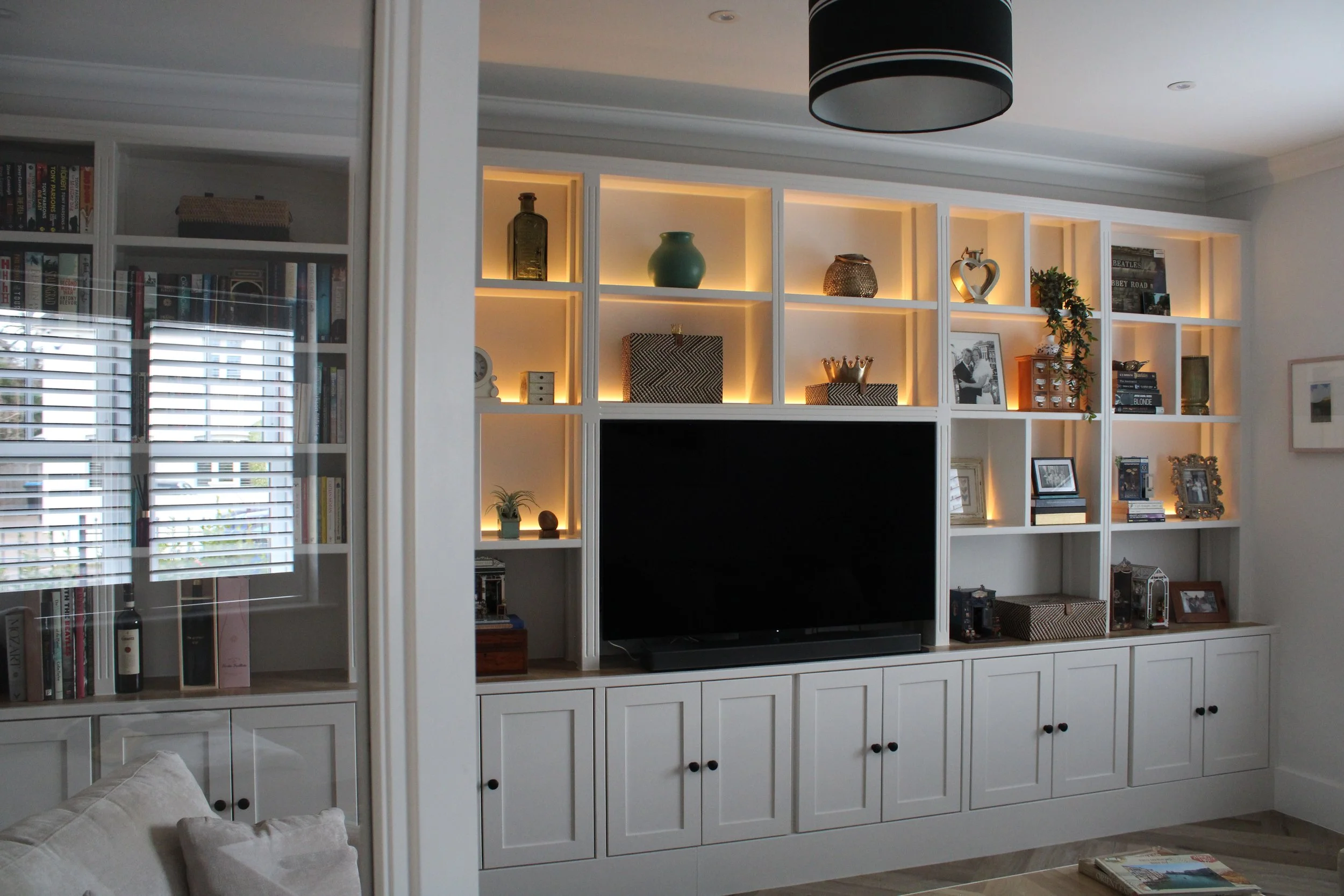 Bespoke, traditional full-wall media unit with integrated warm LED lighting, open shelving, and shaker-style cabinets