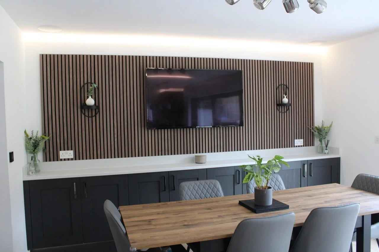 A modern dining room with a wall-mounted flat-screen TV on a wooden accent wall with two wall-mounted shelves holding small vases.