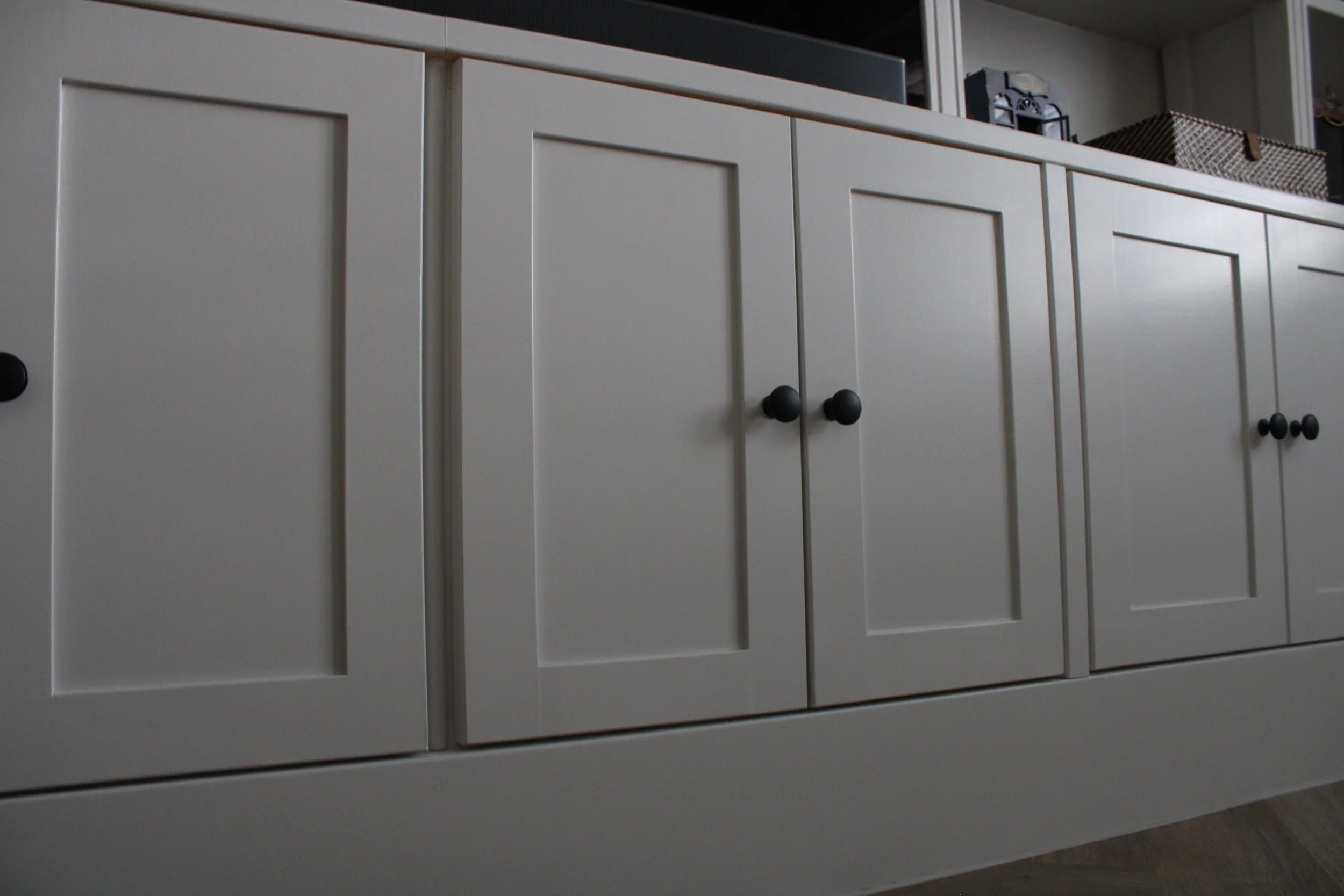 White shaker-style cabinet with black knobs, seen from a low angle.