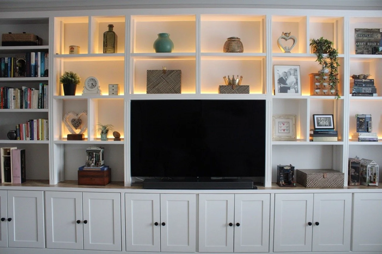Full-width, bespoke media wall with integrated LED-lit shelving, central TV, soundbar and shaker-style cupboard storage.
