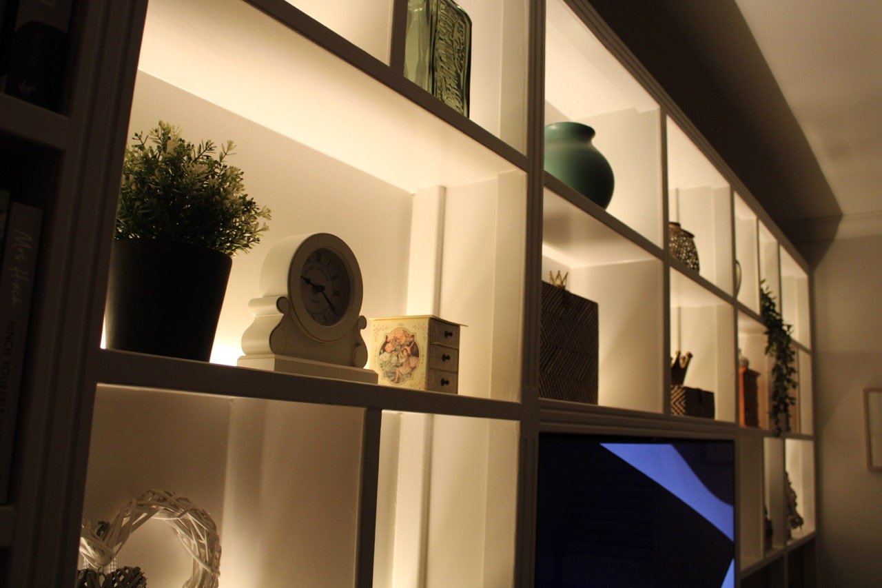 Close-up of bespoke fitted shelving with integrated LED lighting, part of a custom built-in media wall with storage.
