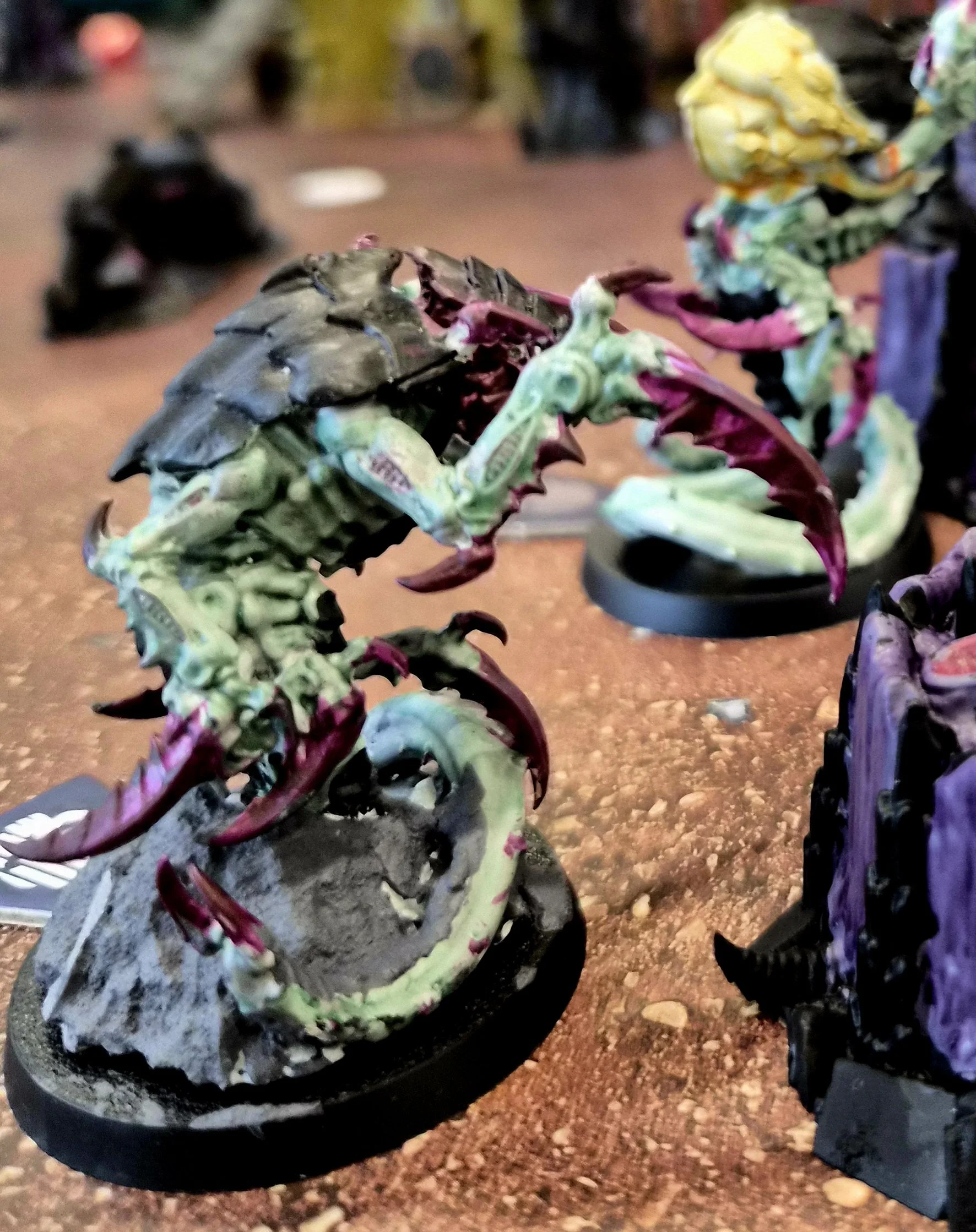 Kill Team model of a Ravener with a black and green body, red claws, and purple accents, placed on a round black base.