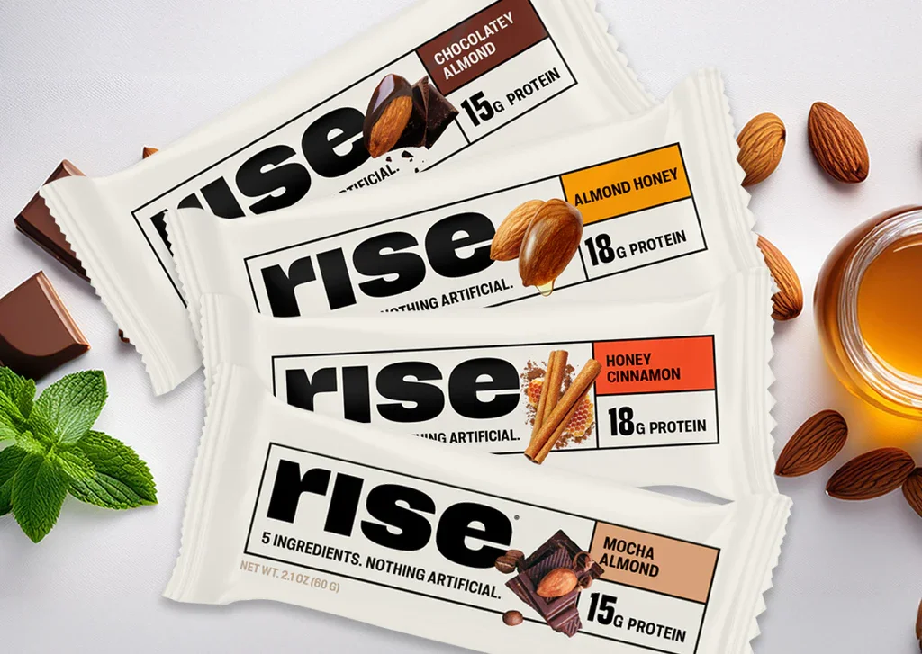 Four rice protein snack bars with different flavors: chocolate almond, almond honey, honey cinnamon, and mocha almond, with ingredients and protein content, surrounded by almonds, honey jar, chocolate square, and mint leaves.