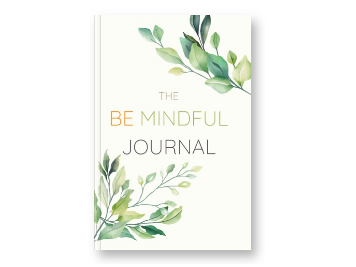 A book titled "The Be Mindful Journal" with a white cover decorated with watercolor green leafy illustrations.