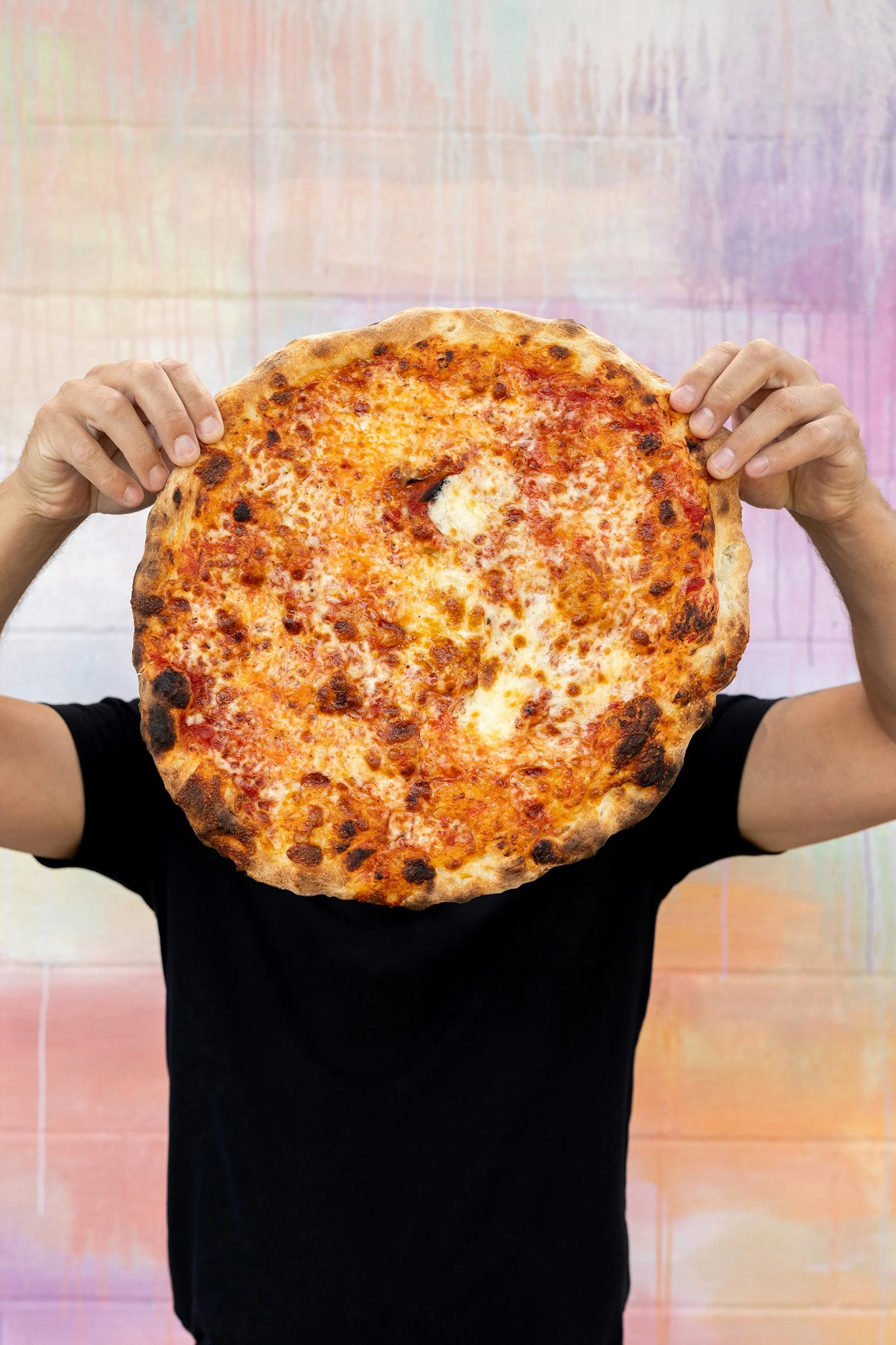 Person holding a large cheese pizza in front of their face.