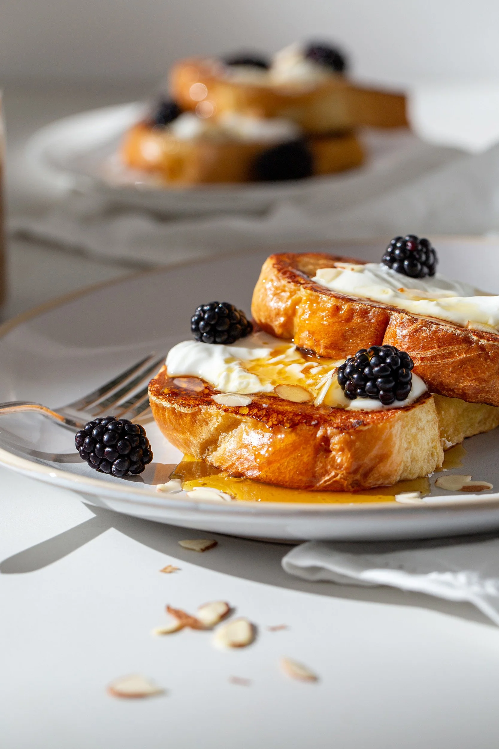 French toast topped with whipped cream, blackberries, and syrup on a white plate with a fork.