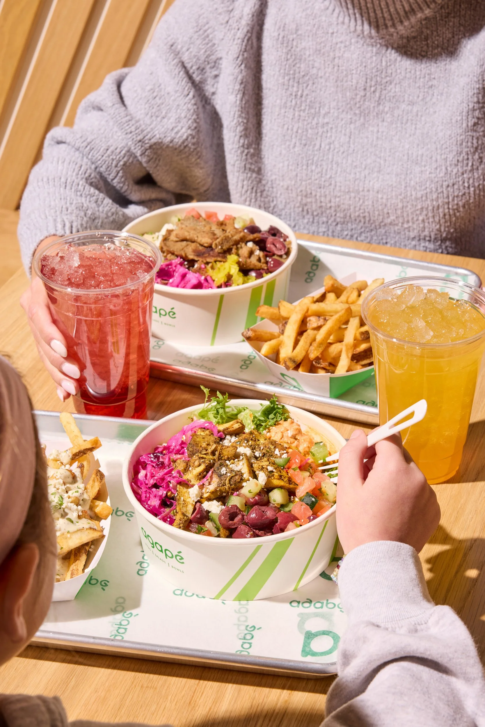 People eating salads, fries, and drinking colorful beverages at a restaurant table.