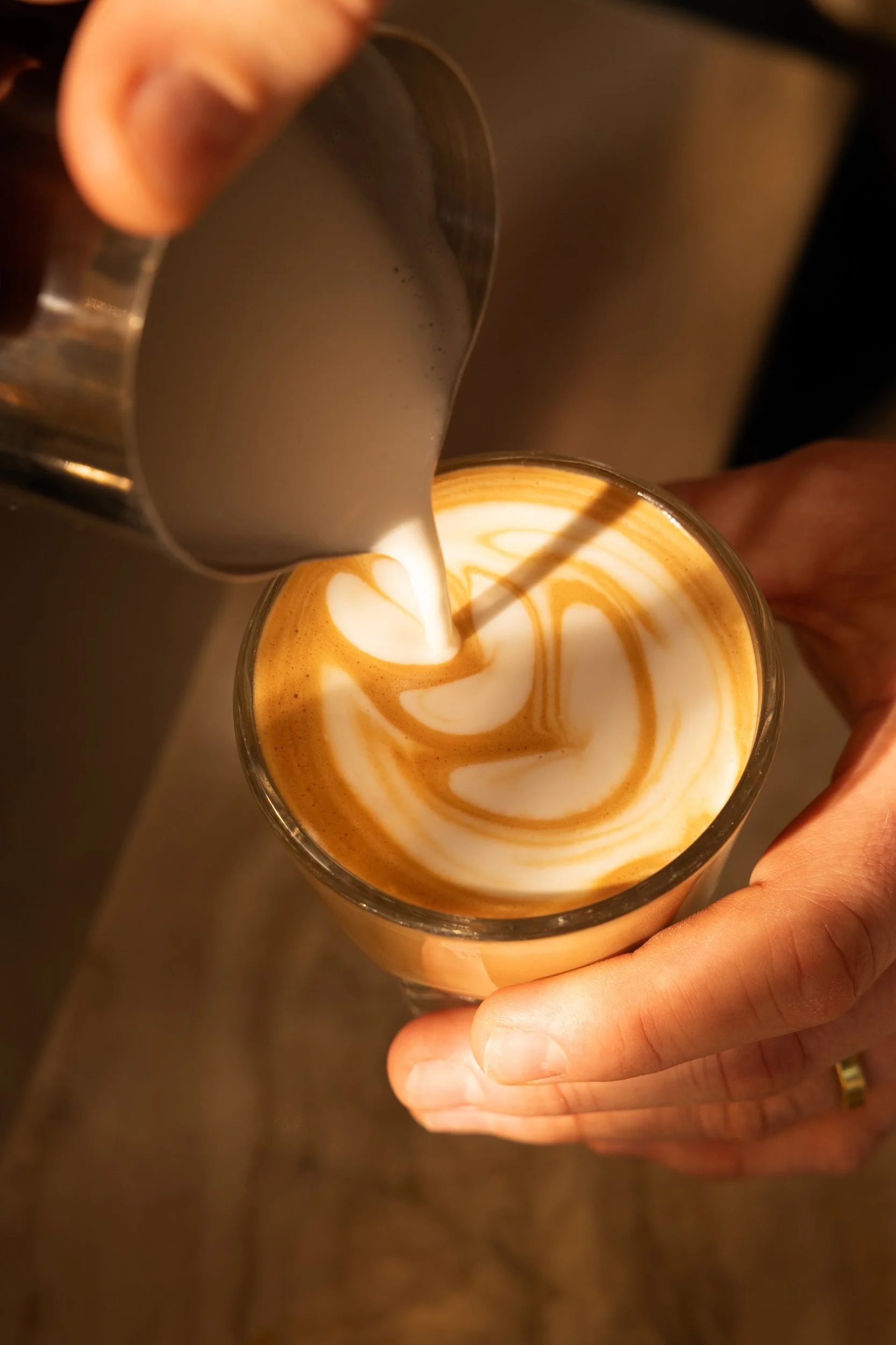 Barista pouring steamed milk into a cup to create latte art with a swirl pattern.