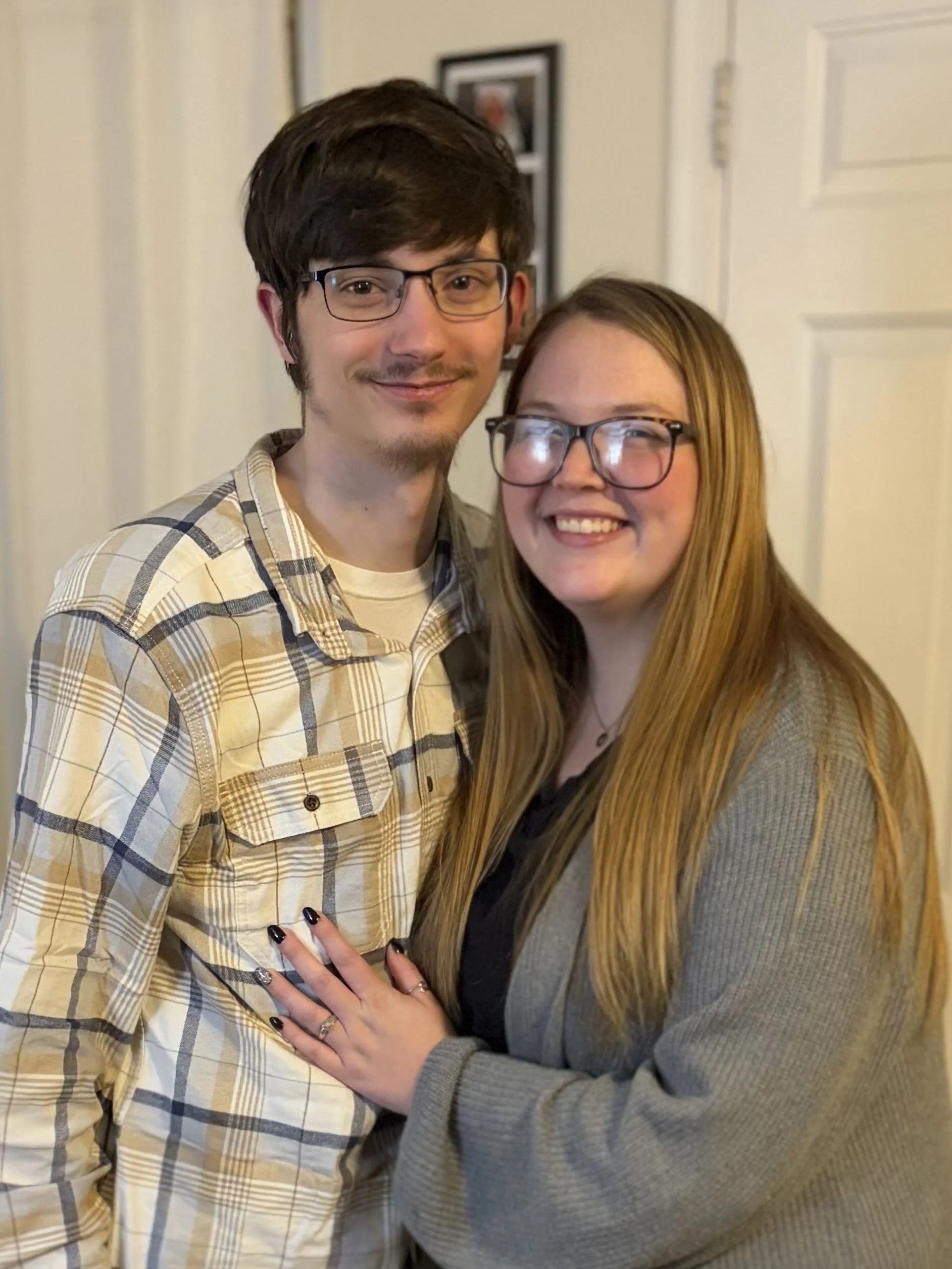 A young man and woman with glasses smiling and posing together indoors.