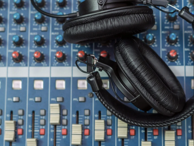 Black headphones placed on a professional audio mixing console with colorful knobs and sliders.
