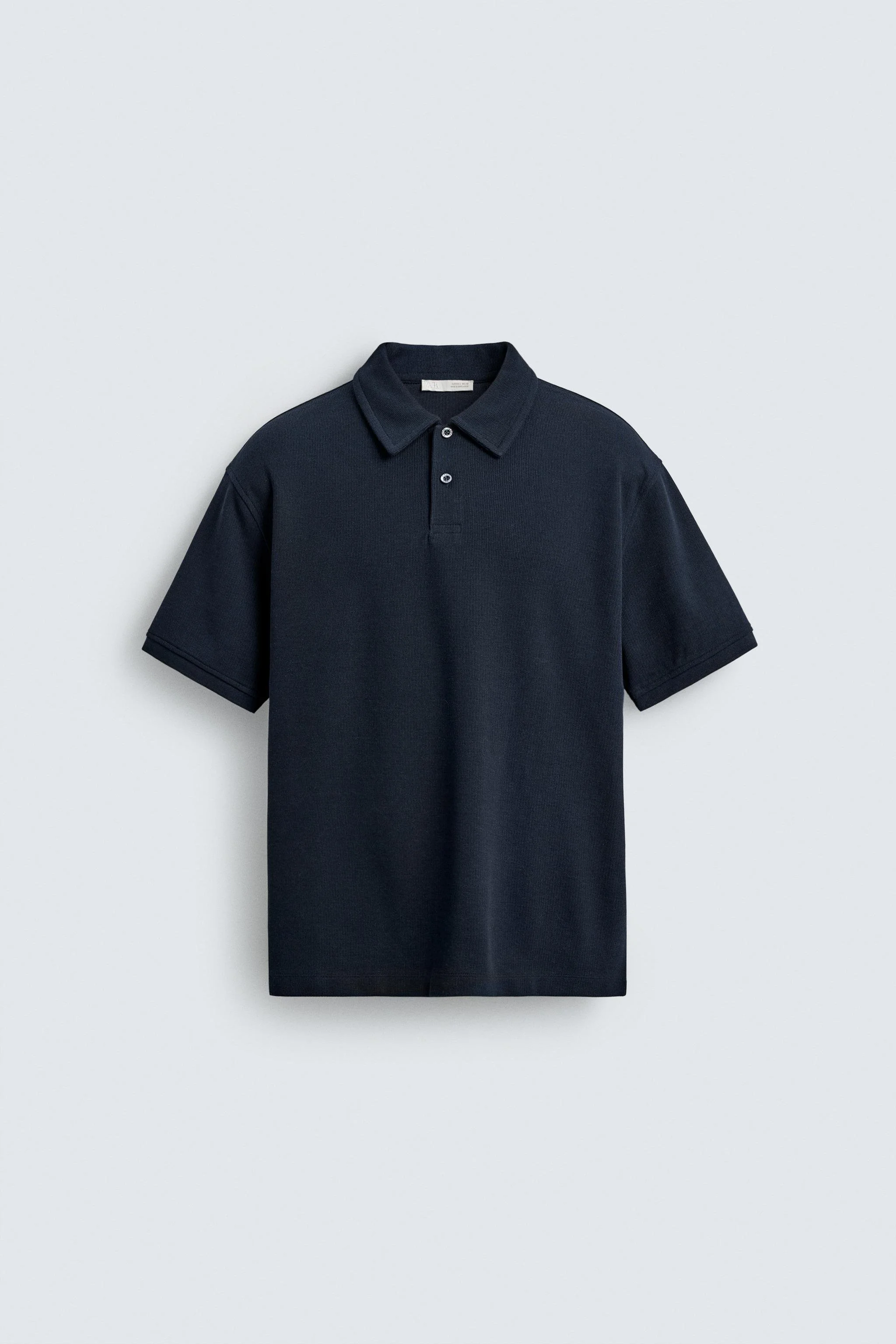 A navy blue short-sleeve polo shirt hanging on a wall