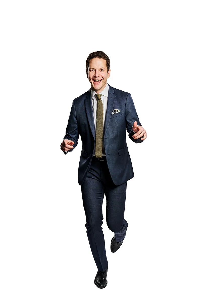 A man in a navy suit and gold tie running and smiling